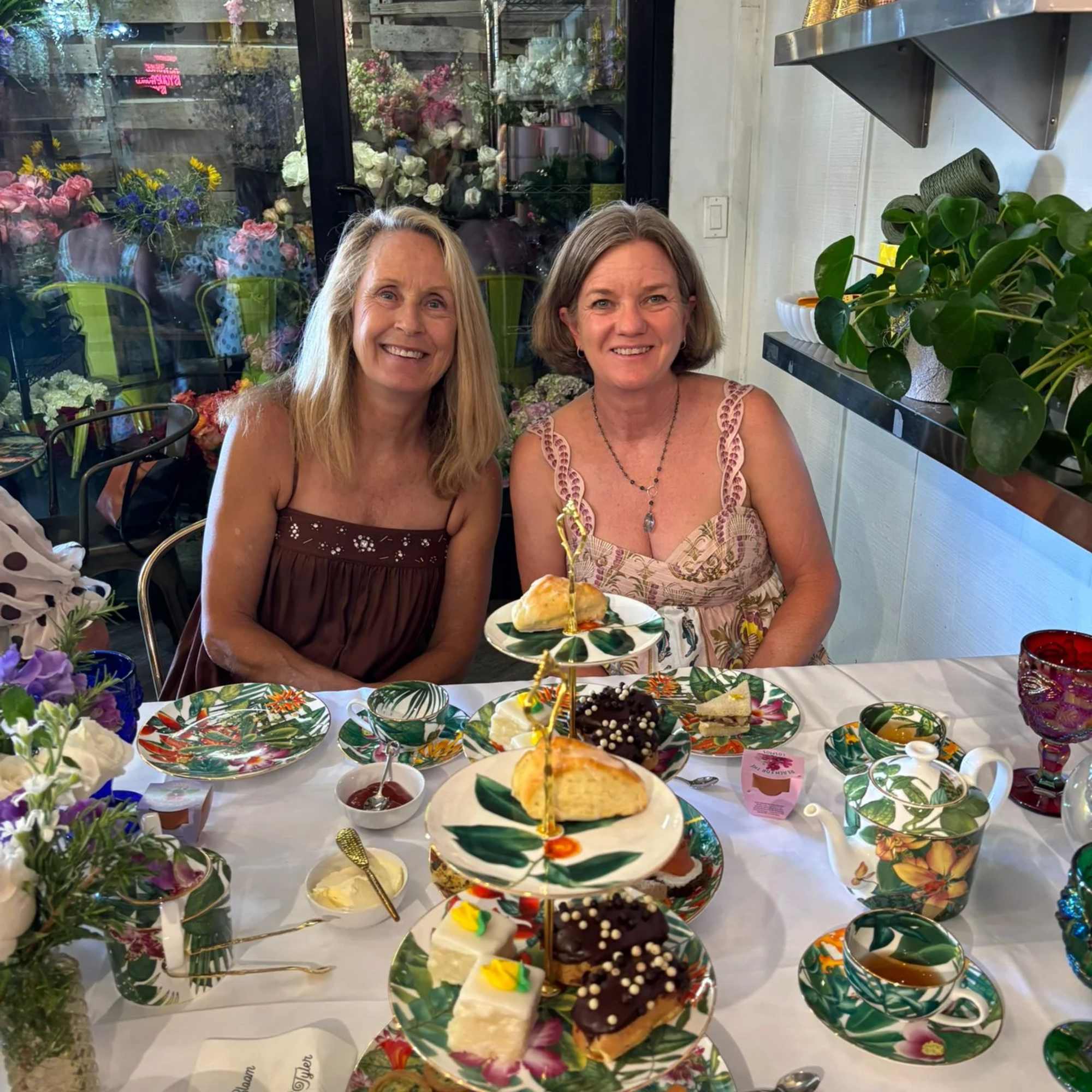 Two women seated at a table with floral-patterned tea service and desserts