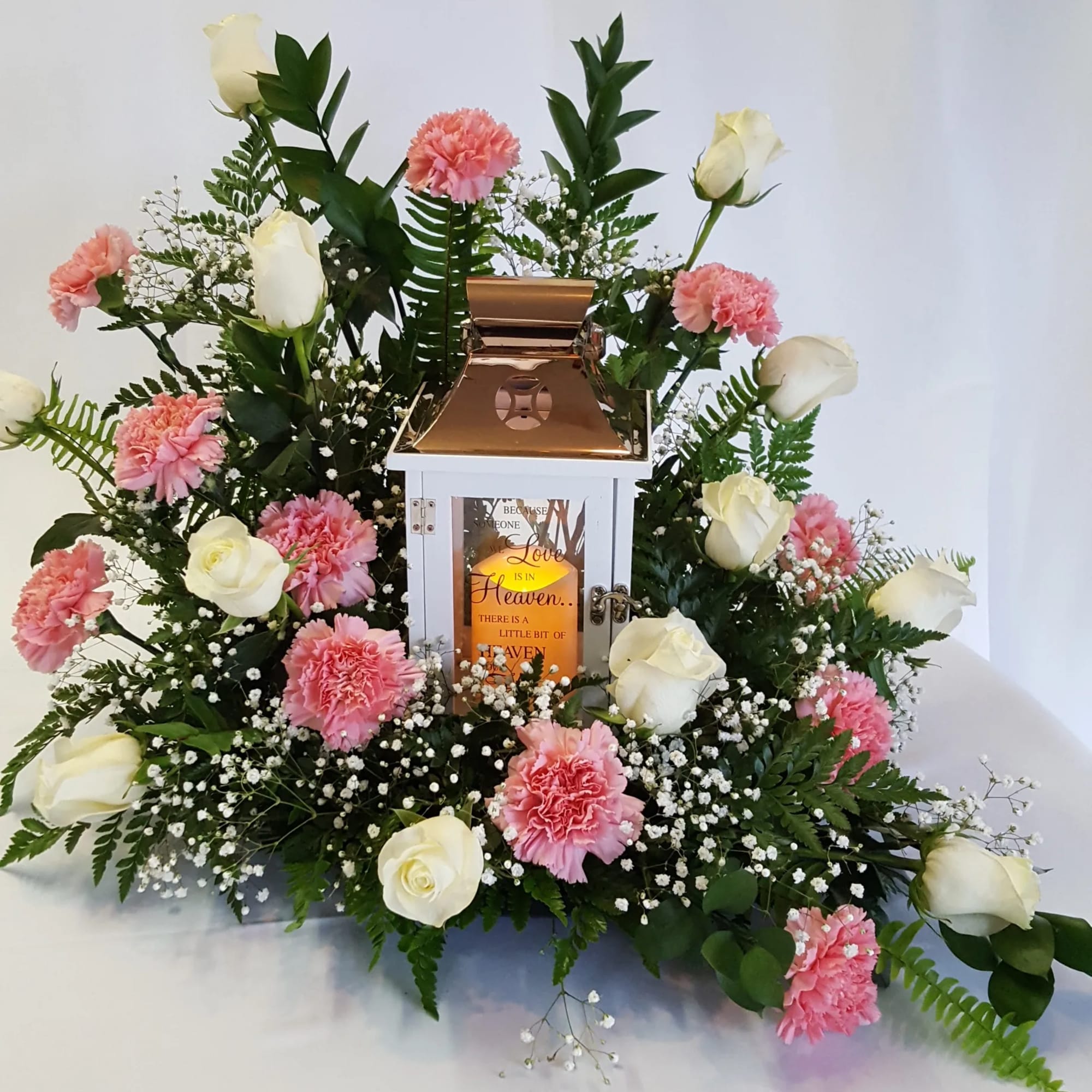 White roses and pink carnations arranged around a lantern centerpiece