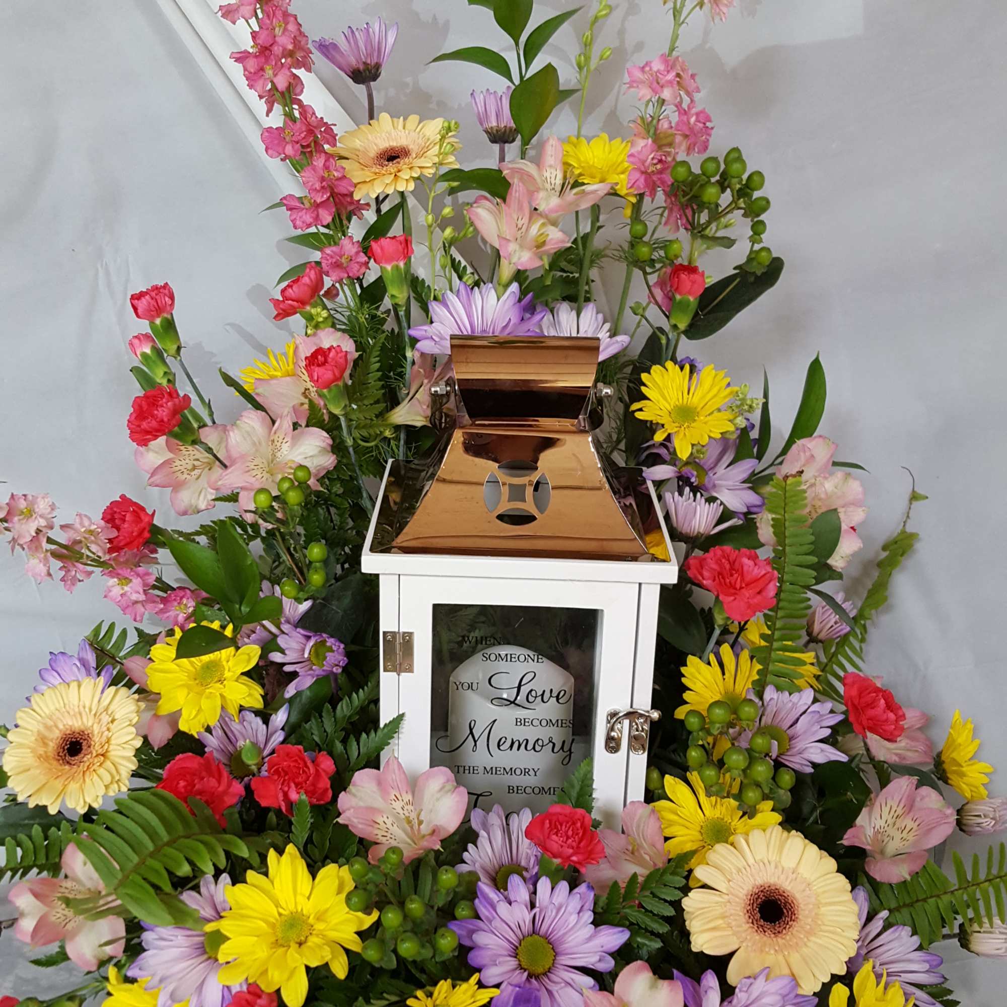 Colorful sympathy floral arrangement around a white lantern with a copper top