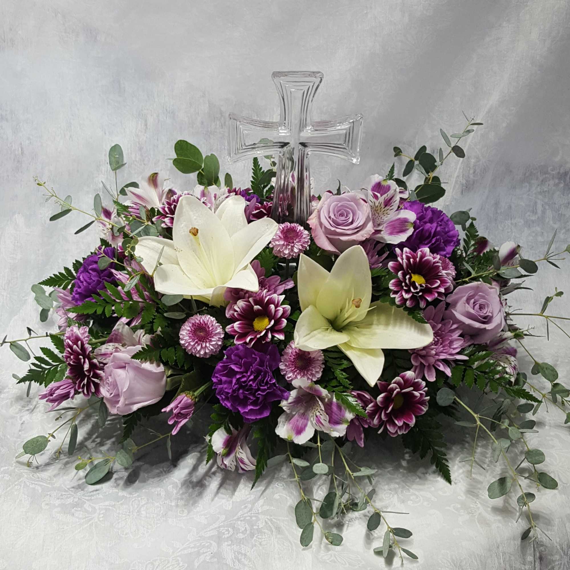 Purple and white floral arrangement with a clear glass cross centerpiece