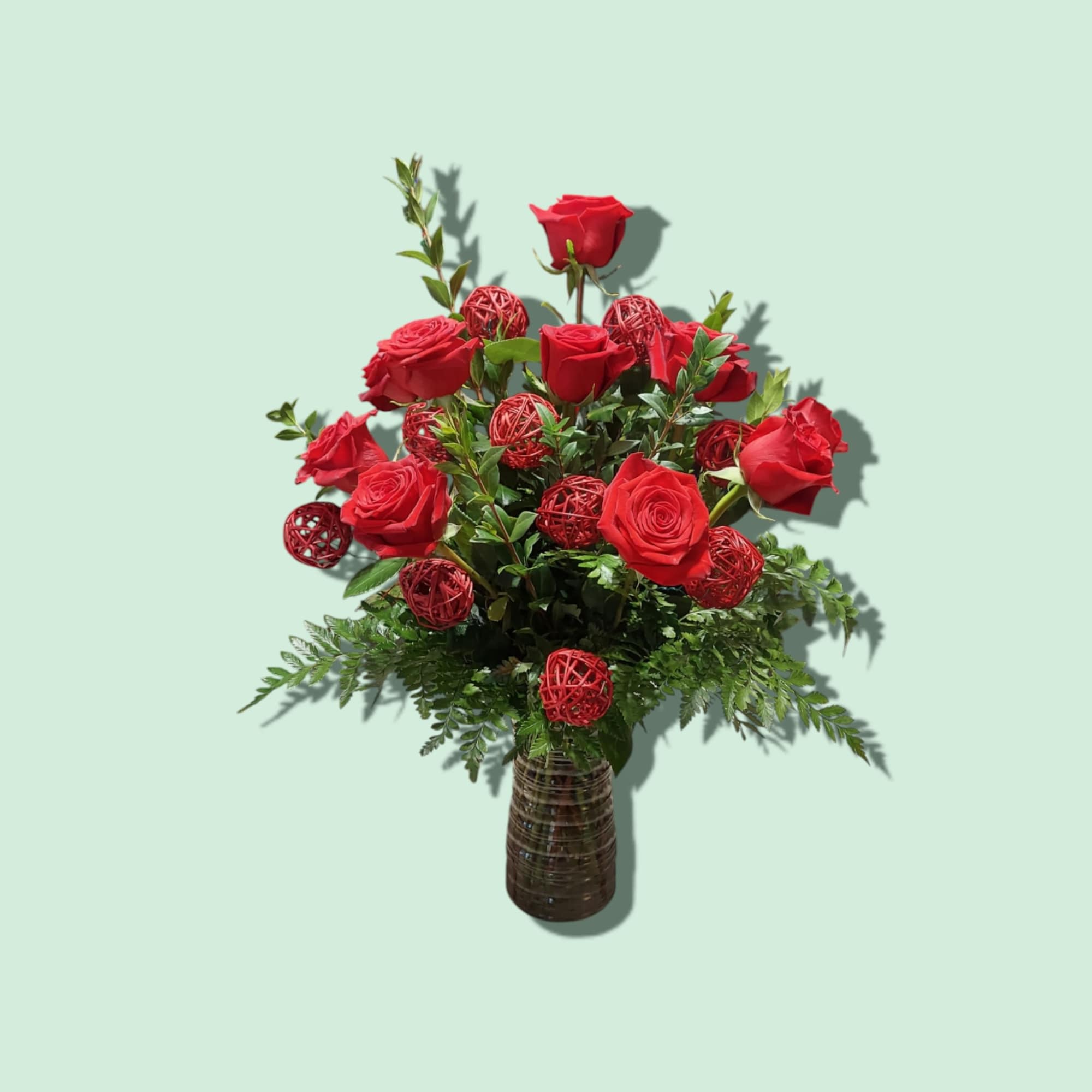 Red roses arranged in a dark vase with red decorative spheres
