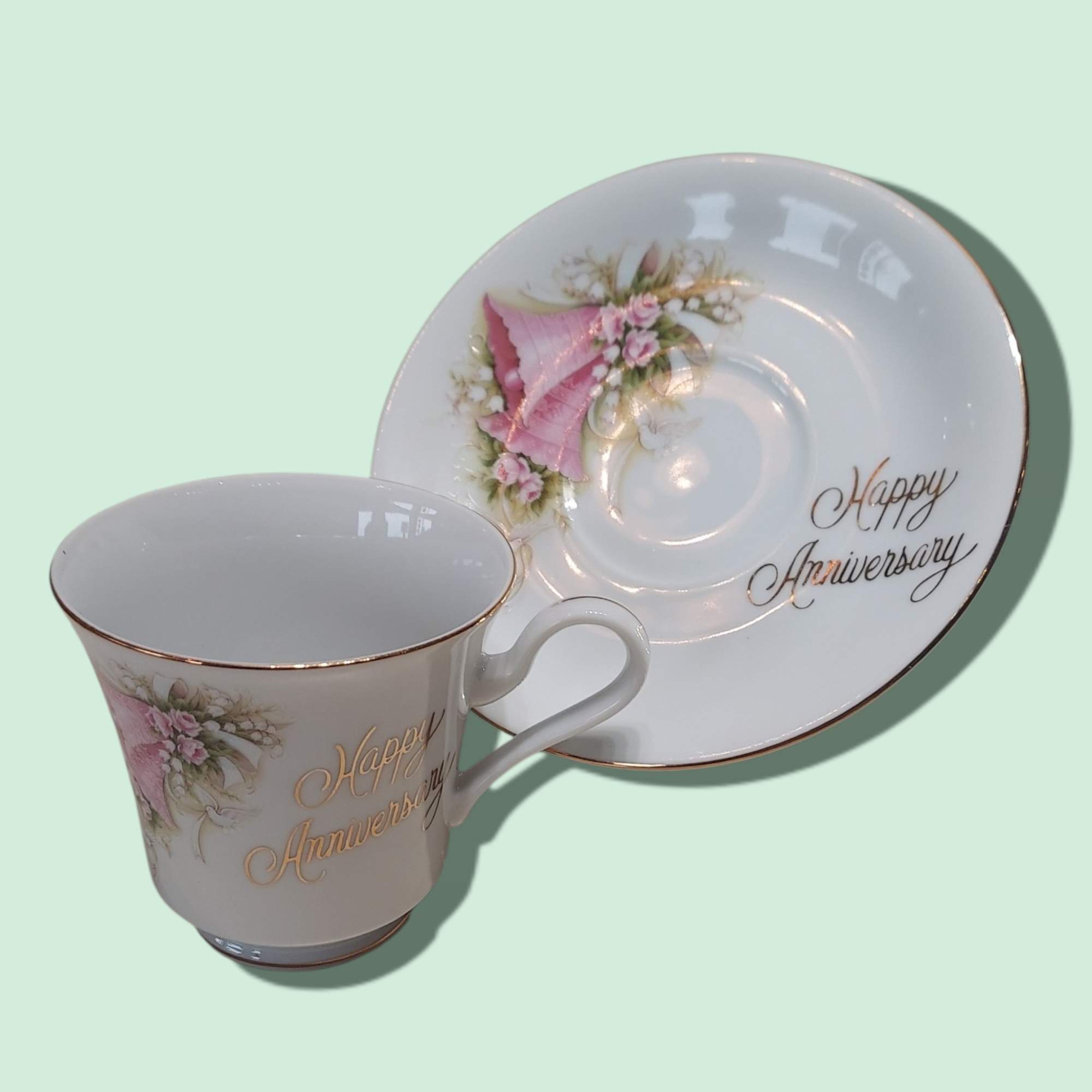 Porcelain teacup and saucer with pink floral decoration and "Happy Anniversary" text
