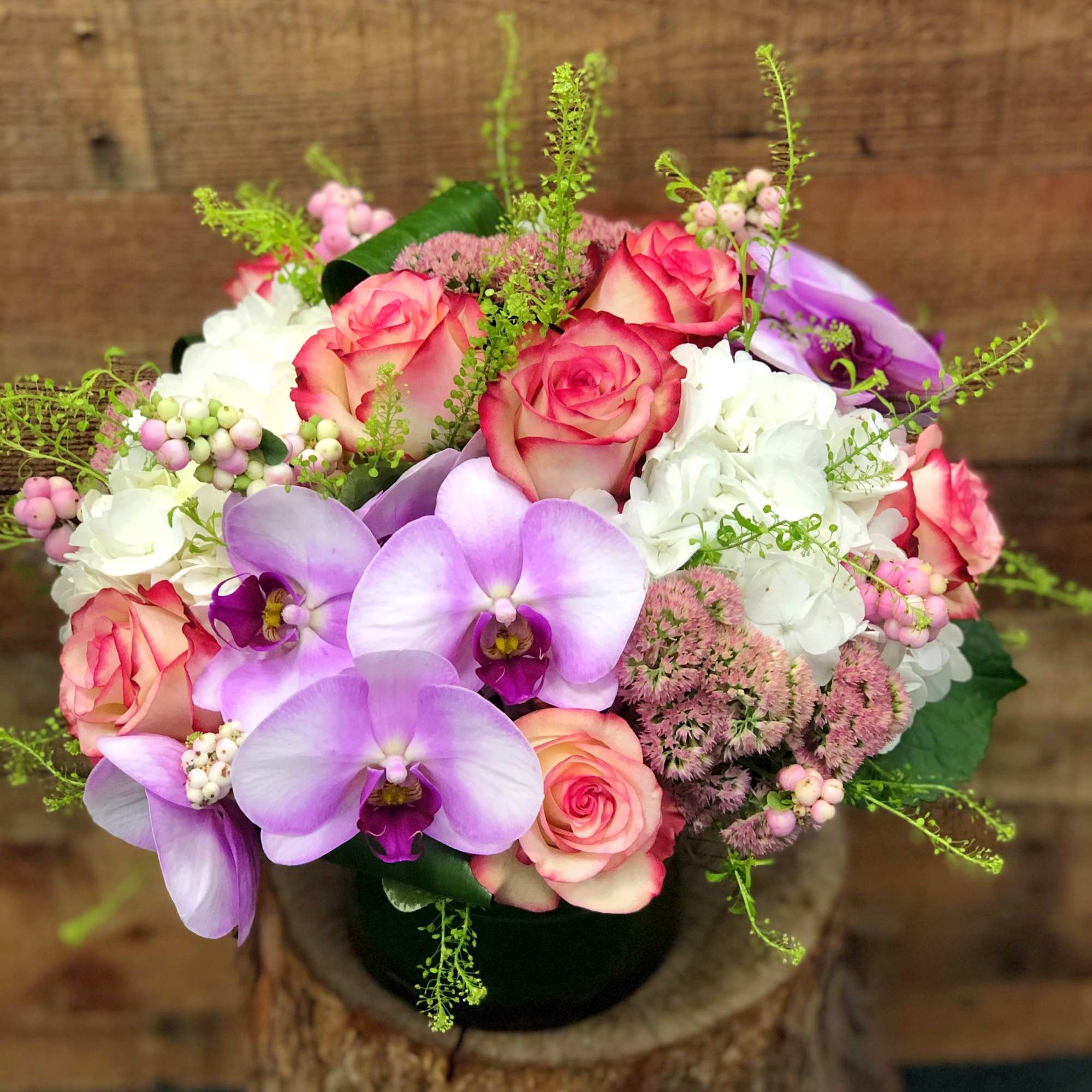 Bouquet of pink roses, lavender orchids, and white hydrangeas in a black vase