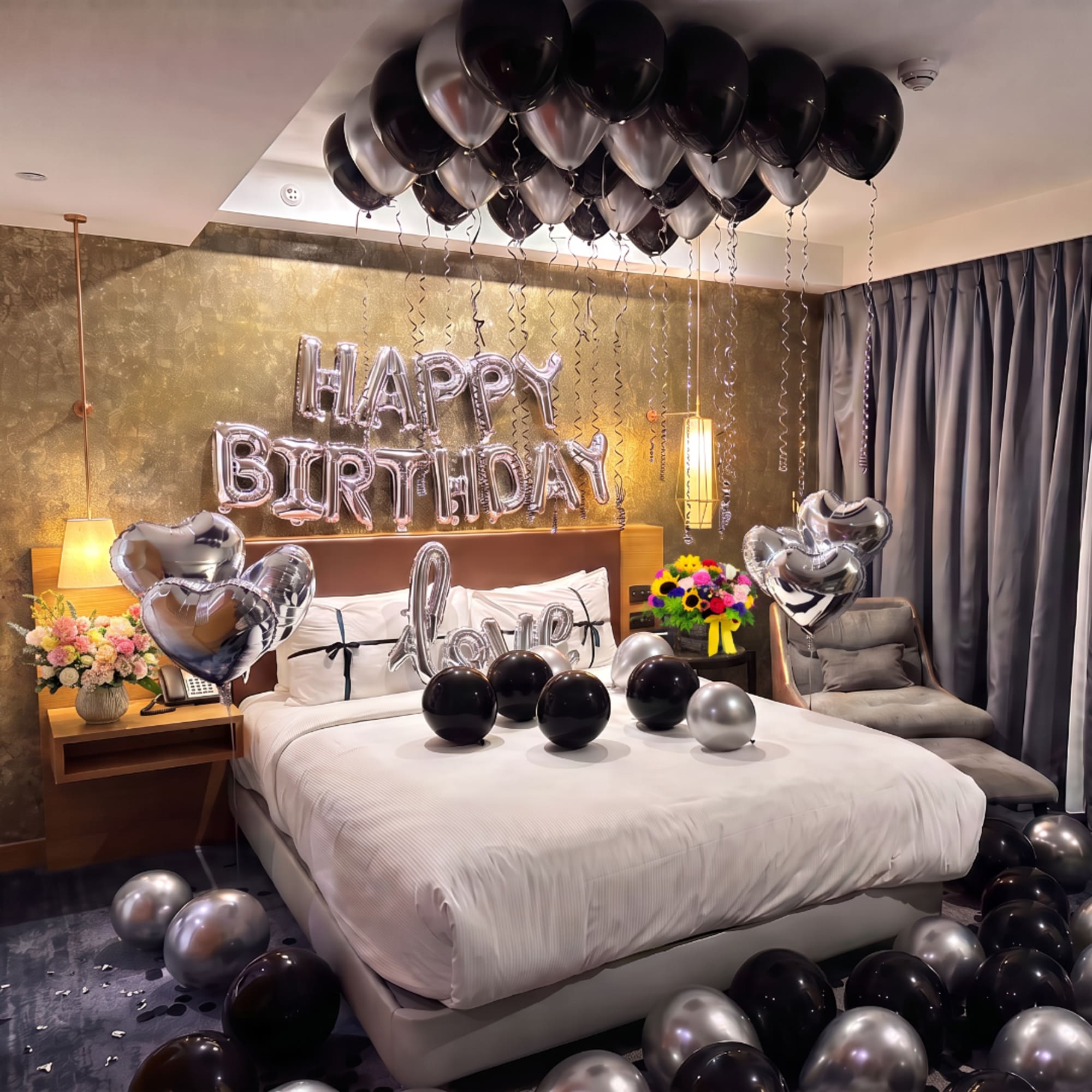 Birthday room decorated with black and silver balloons and heart balloons over a bed