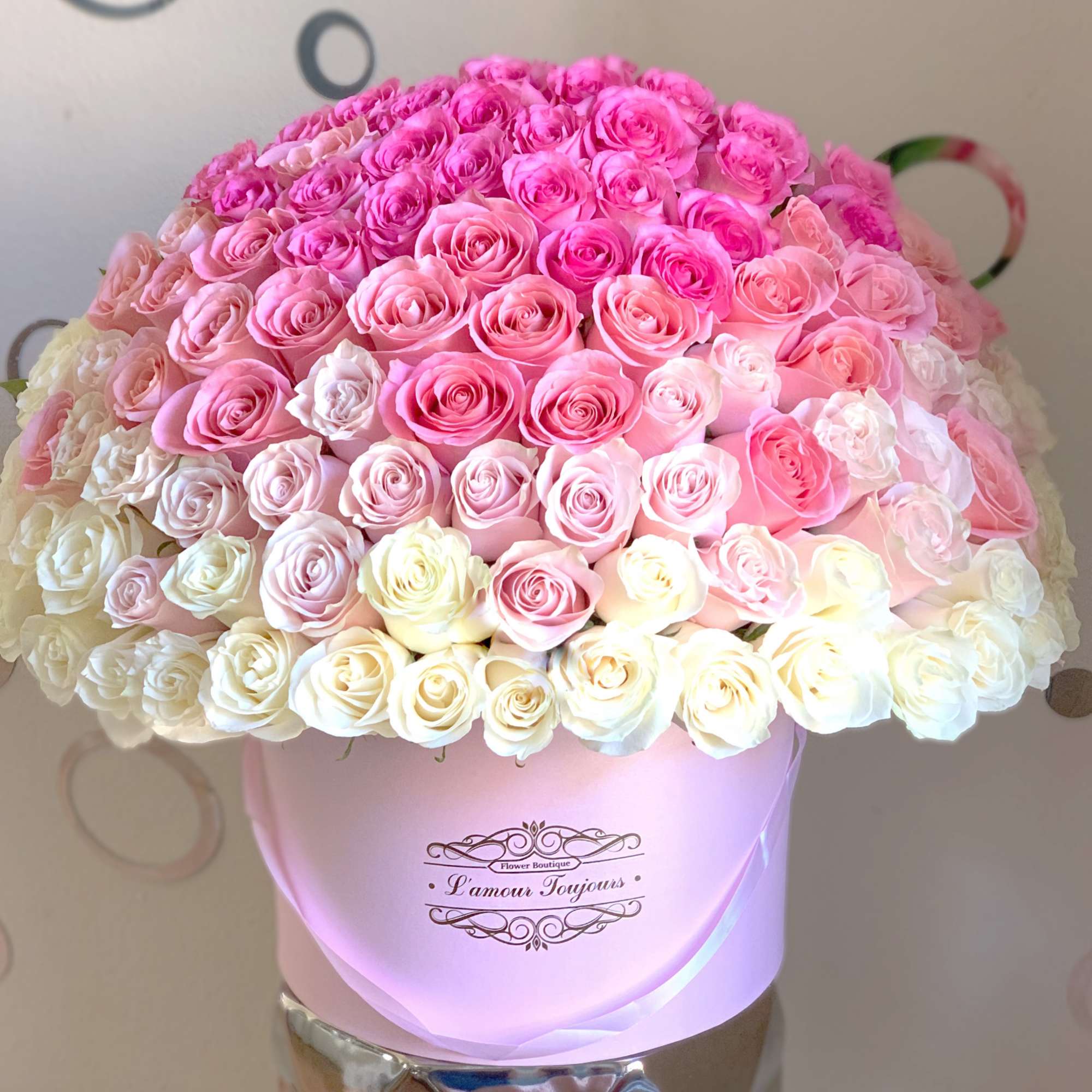 Large dome of pink and cream roses arranged in a round pastel pink hatbox.