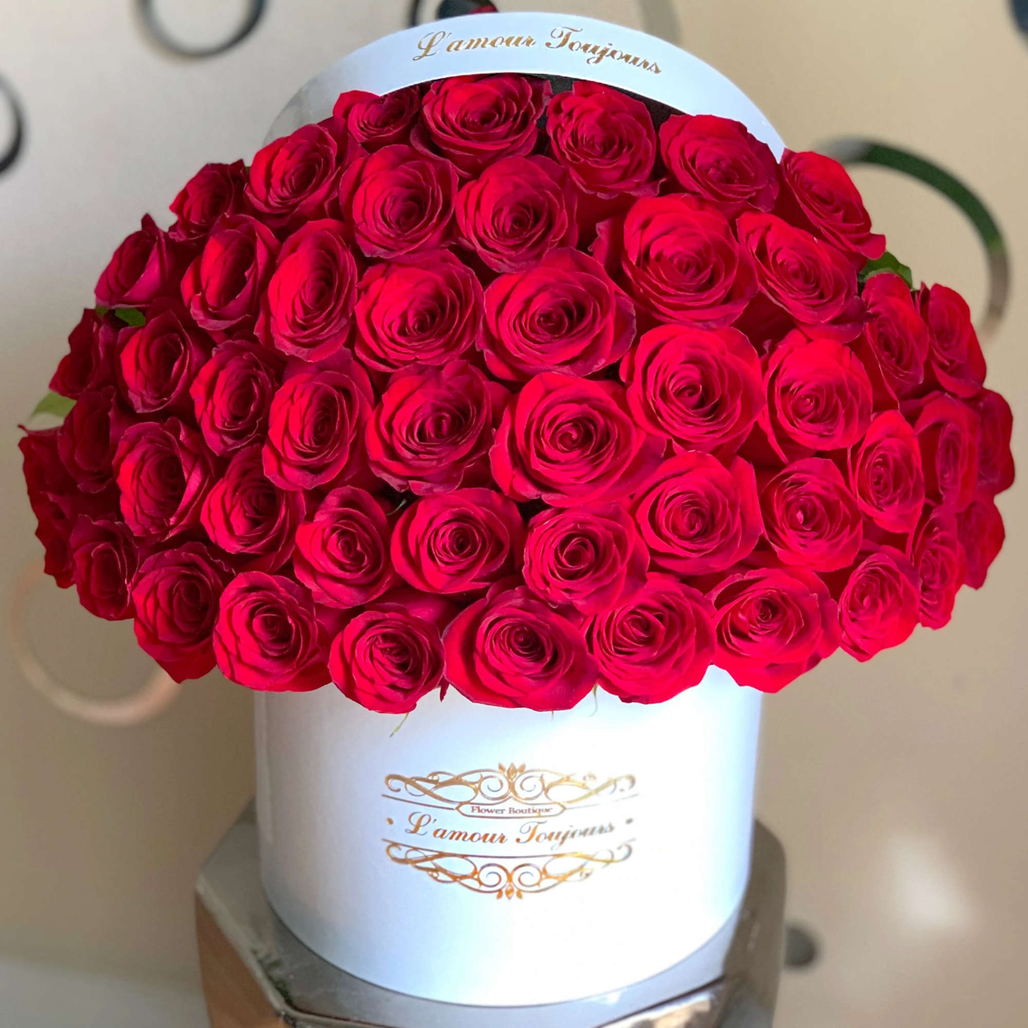 Round white hat box filled with tightly packed red roses and gold script label on the front.