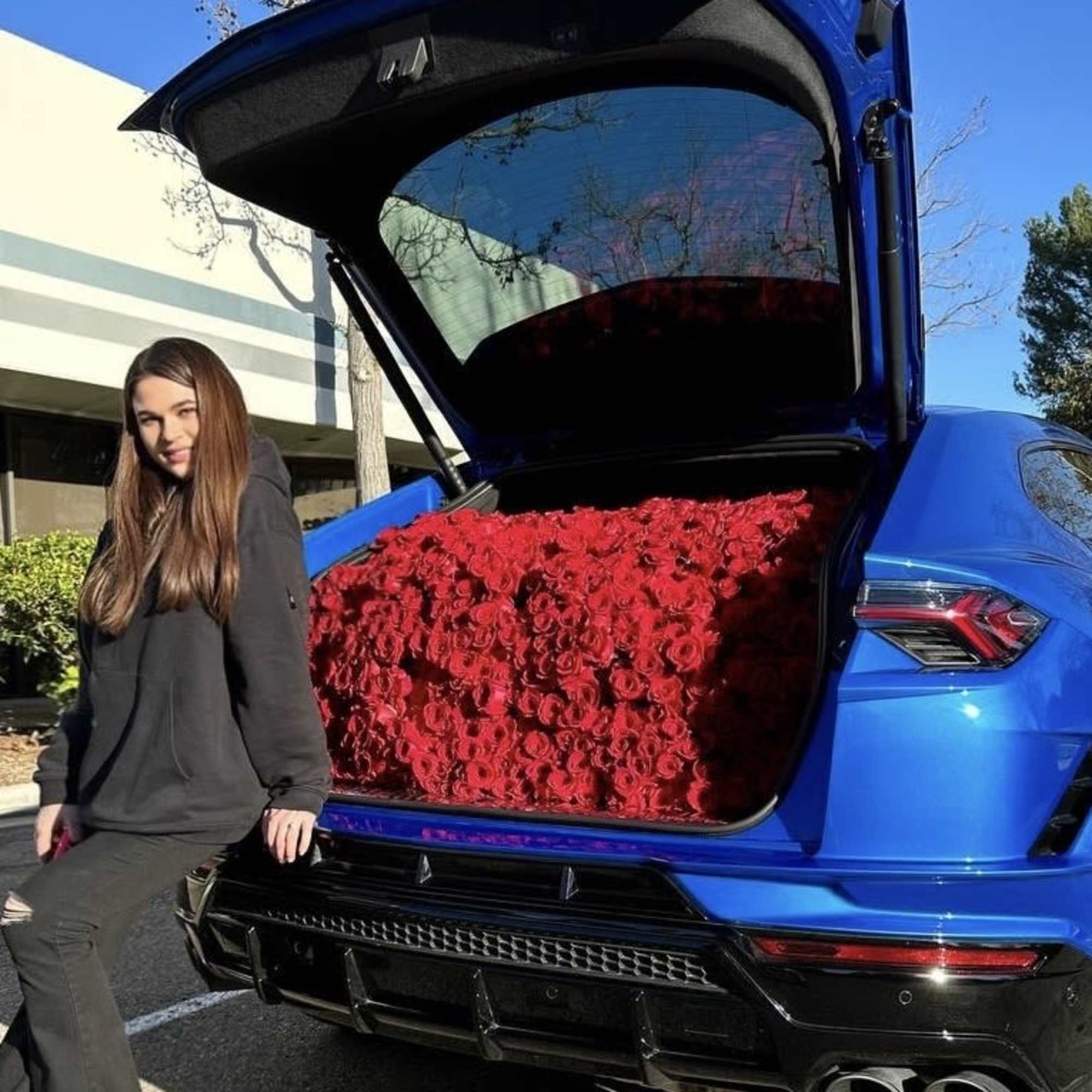 Blue SUV with its trunk filled with red roses beside a woman