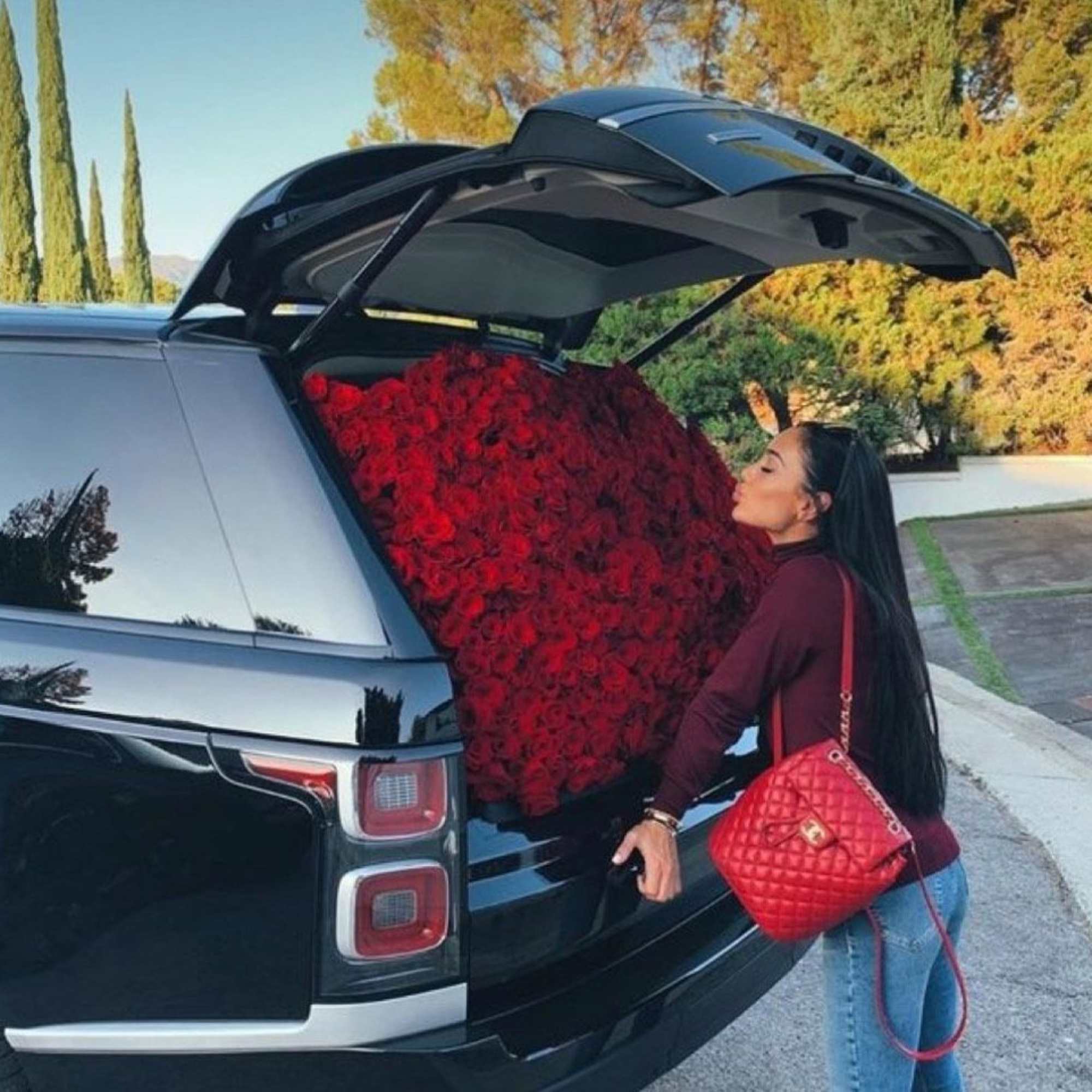 Woman kissing a SUV filled with red roses in the open trunk