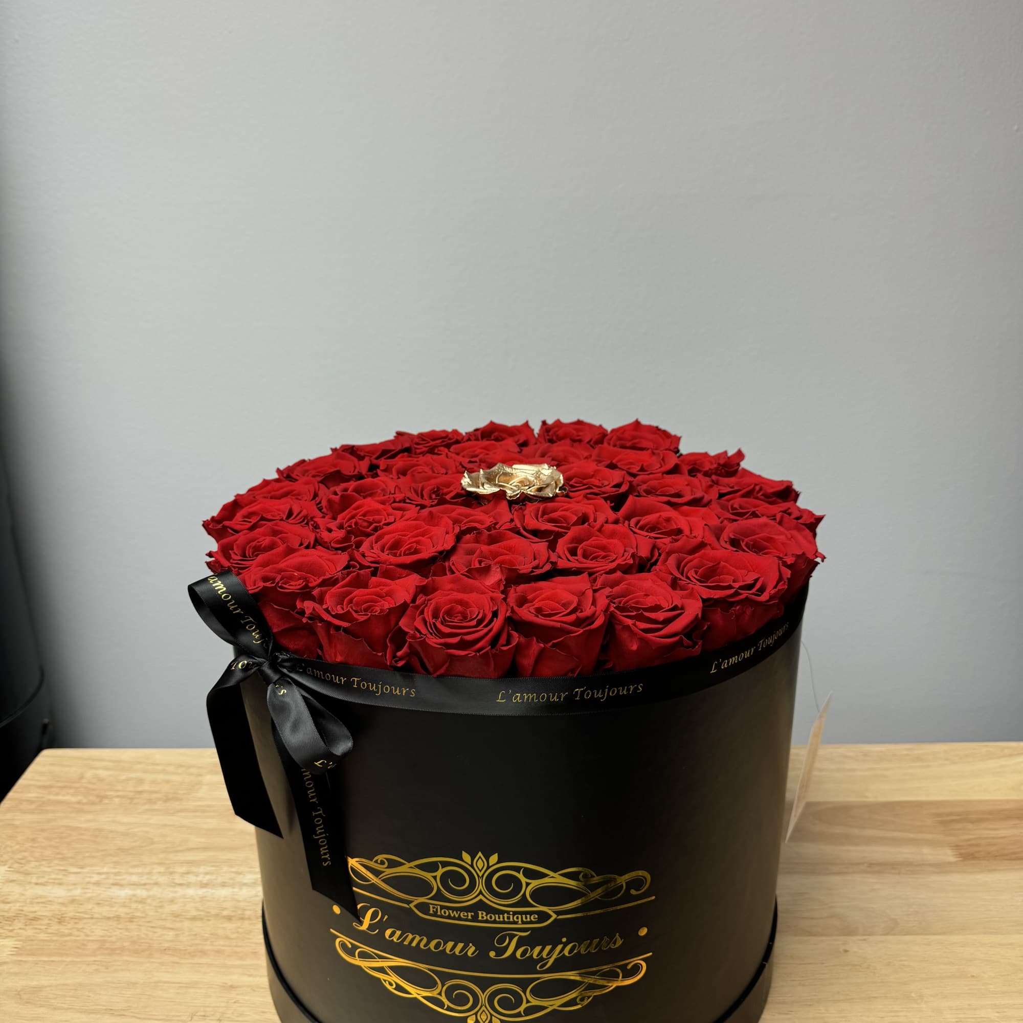 Round black hatbox filled with red roses and one gold rose on a wooden table