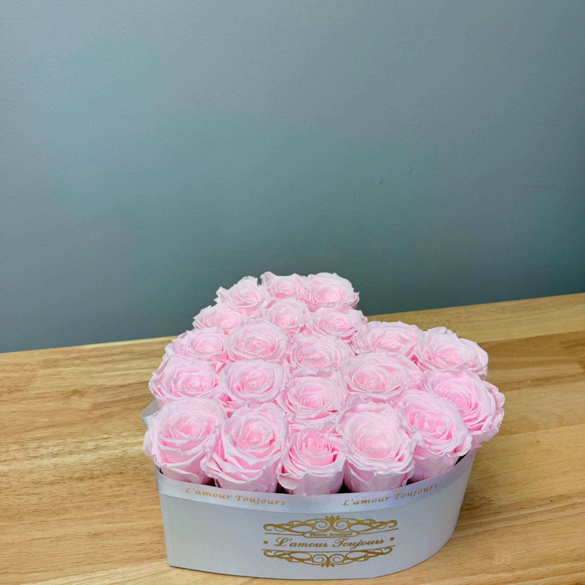 Pink roses arranged in a white heart-shaped box on a wooden table