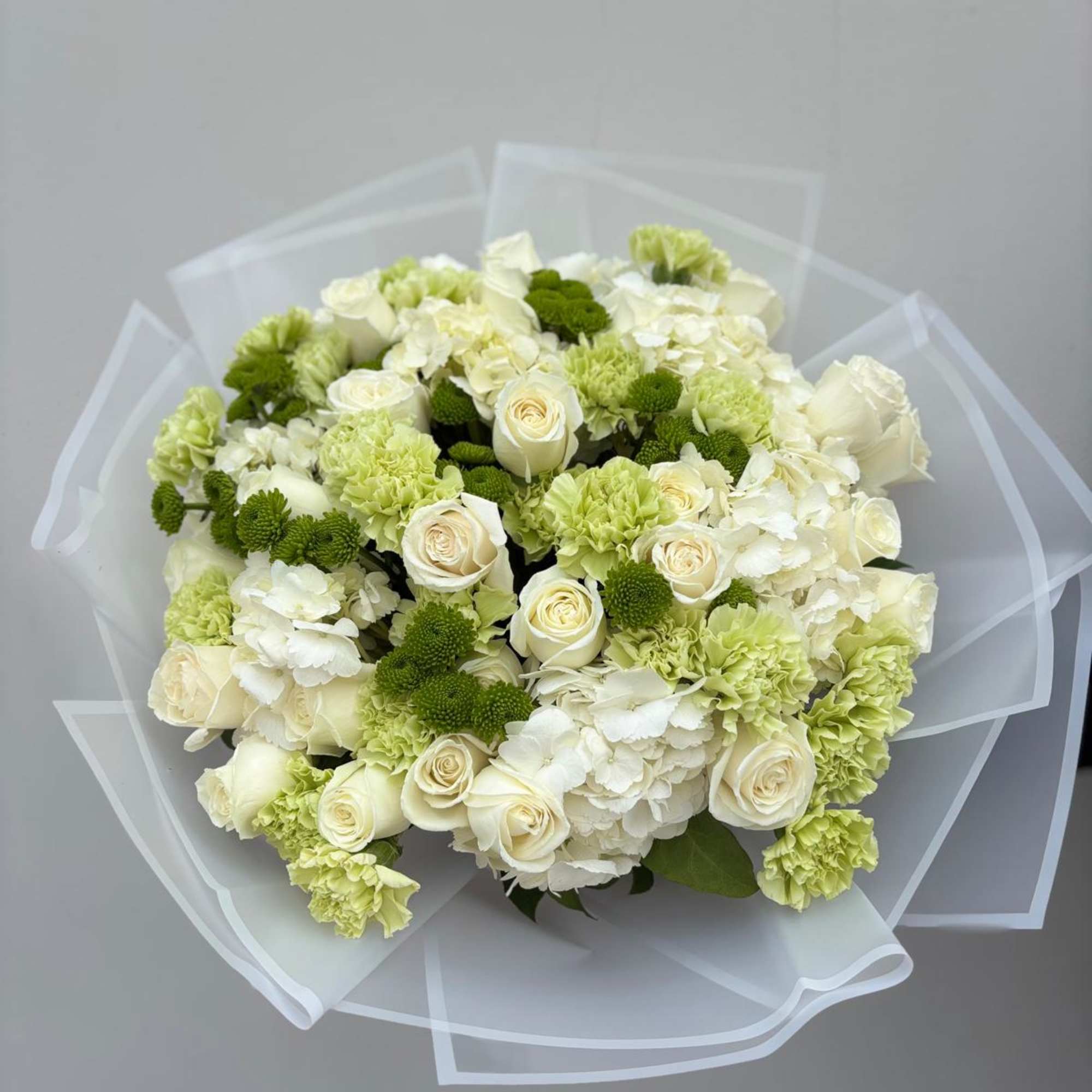 Bouquet of white roses, hydrangeas, and green carnations wrapped in clear paper