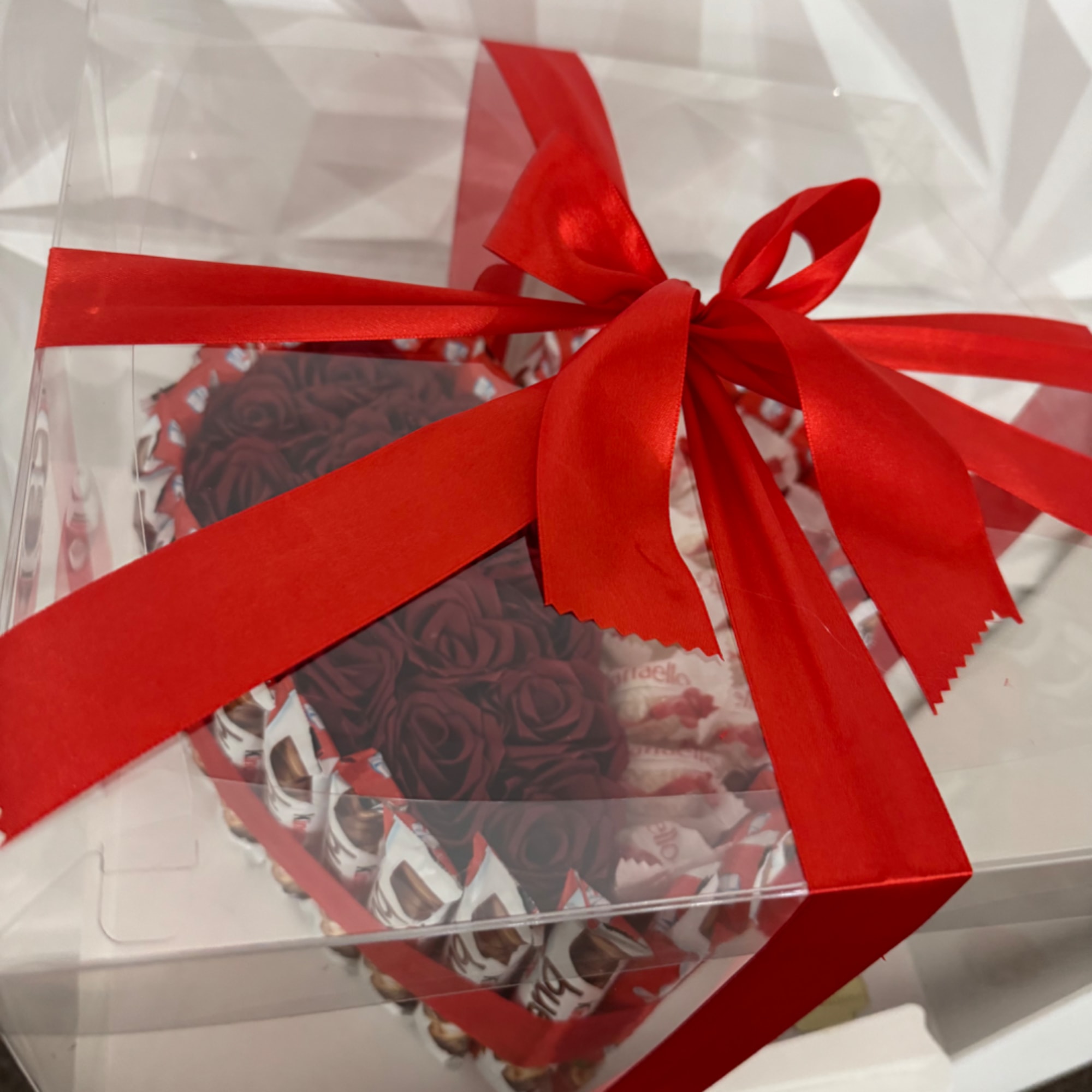 Heart-shaped gift box with red roses and chocolates, tied with a red ribbon