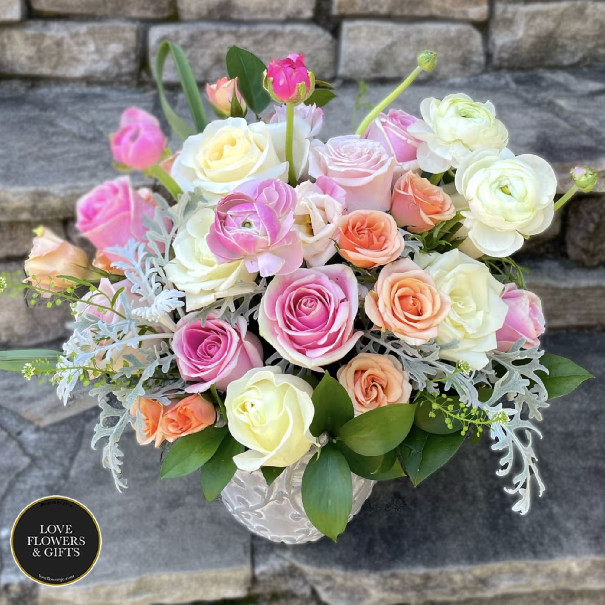 Pastel roses and ranunculus arranged in a white ceramic vase.