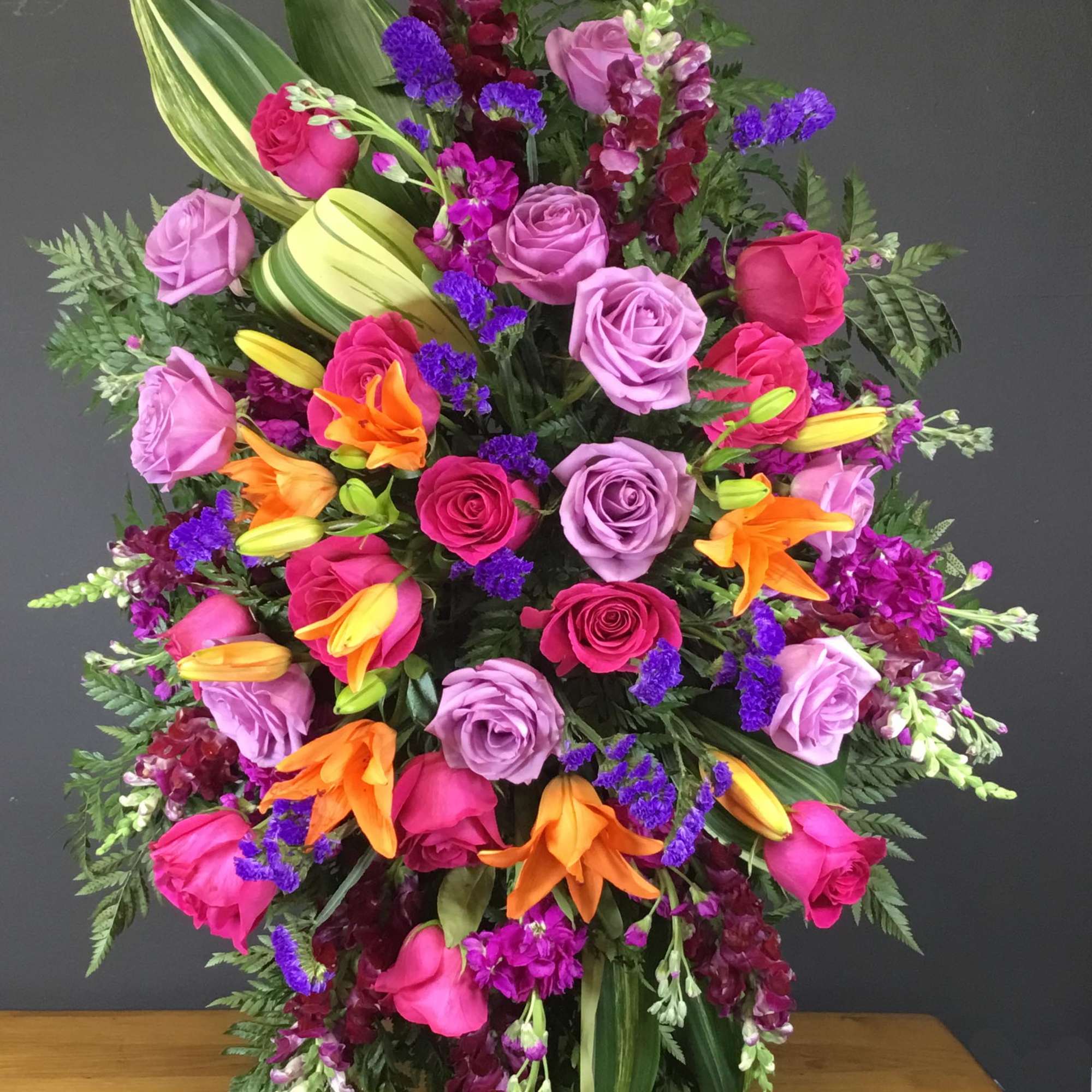 Large mixed floral arrangement with pink and lavender roses, orange lilies, and purple accents