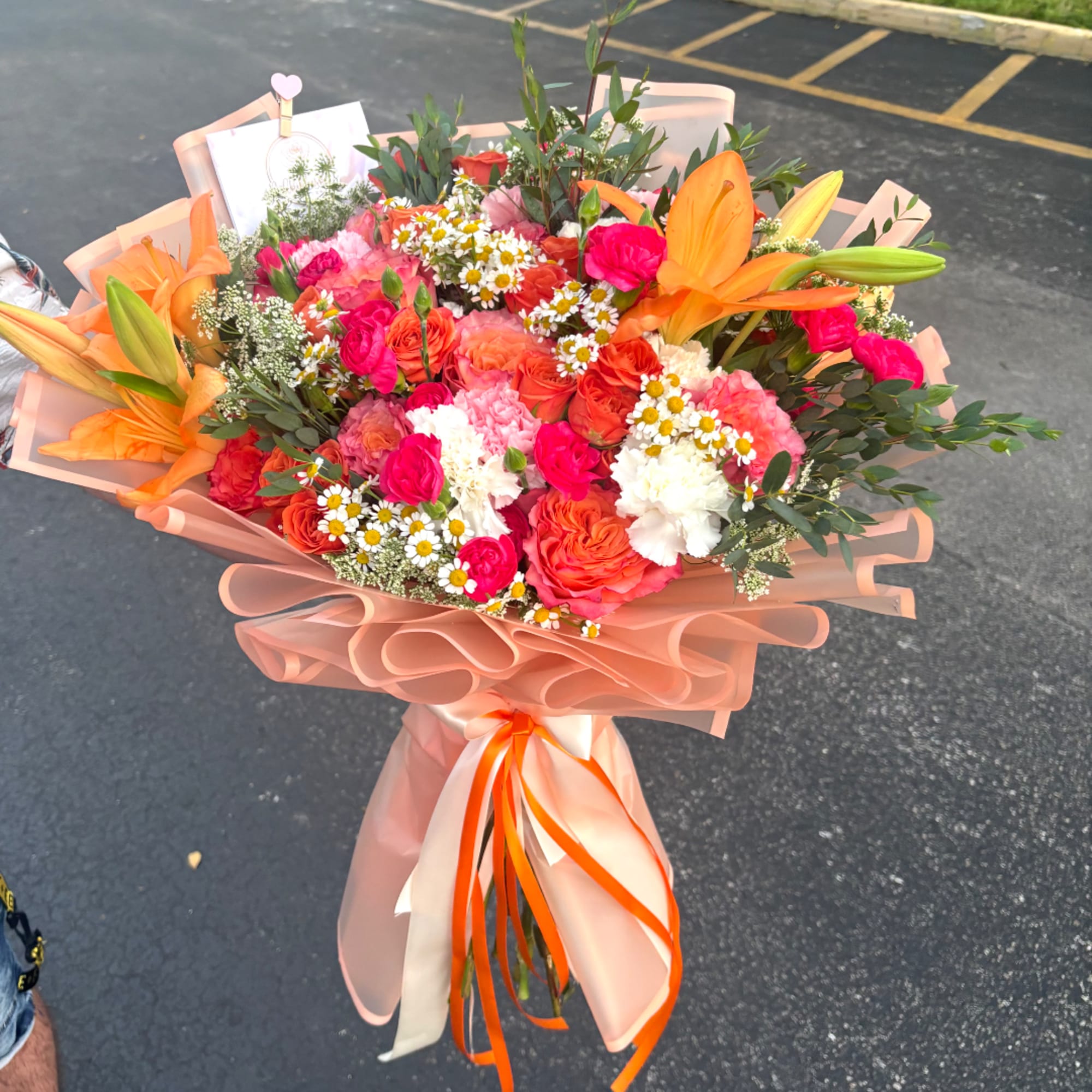Bouquet of orange lilies, pink roses, and white daisies wrapped in peach paper
