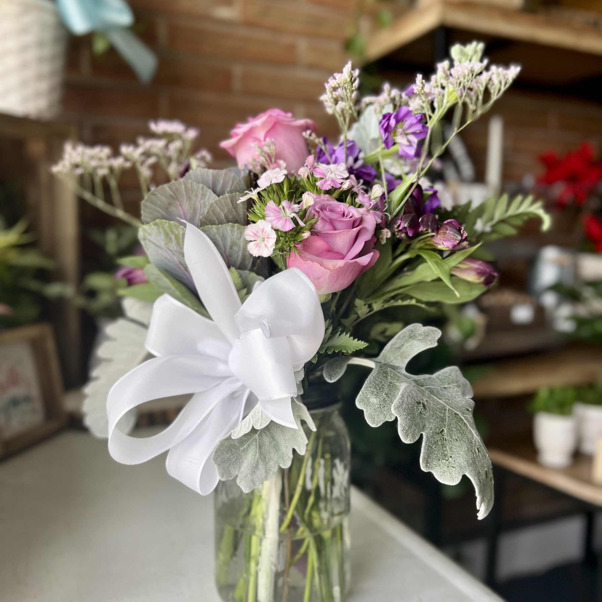 Pink roses and purple flowers in a glass vase with a white ribbon