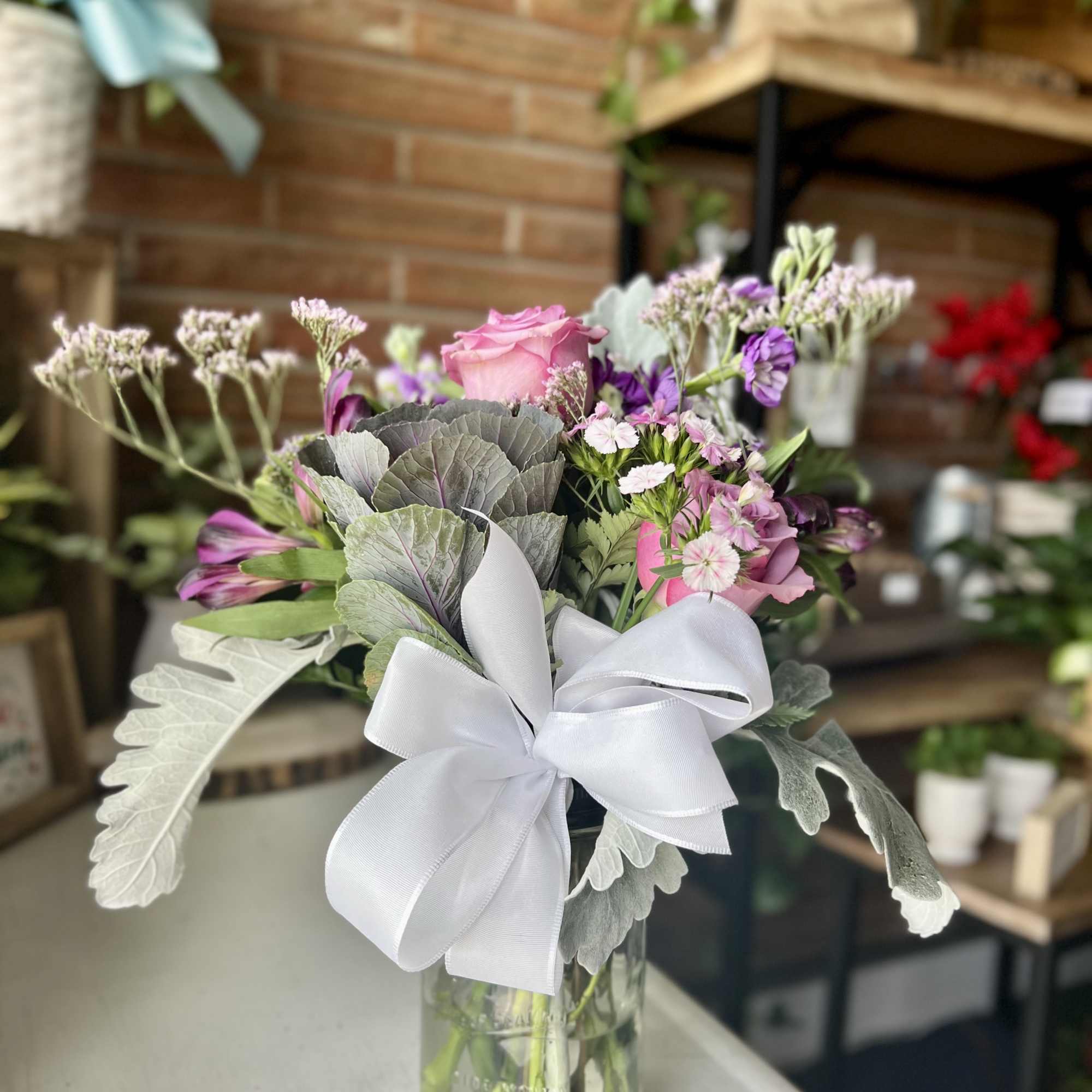 Pink and purple bouquet in a glass vase with a white ribbon
