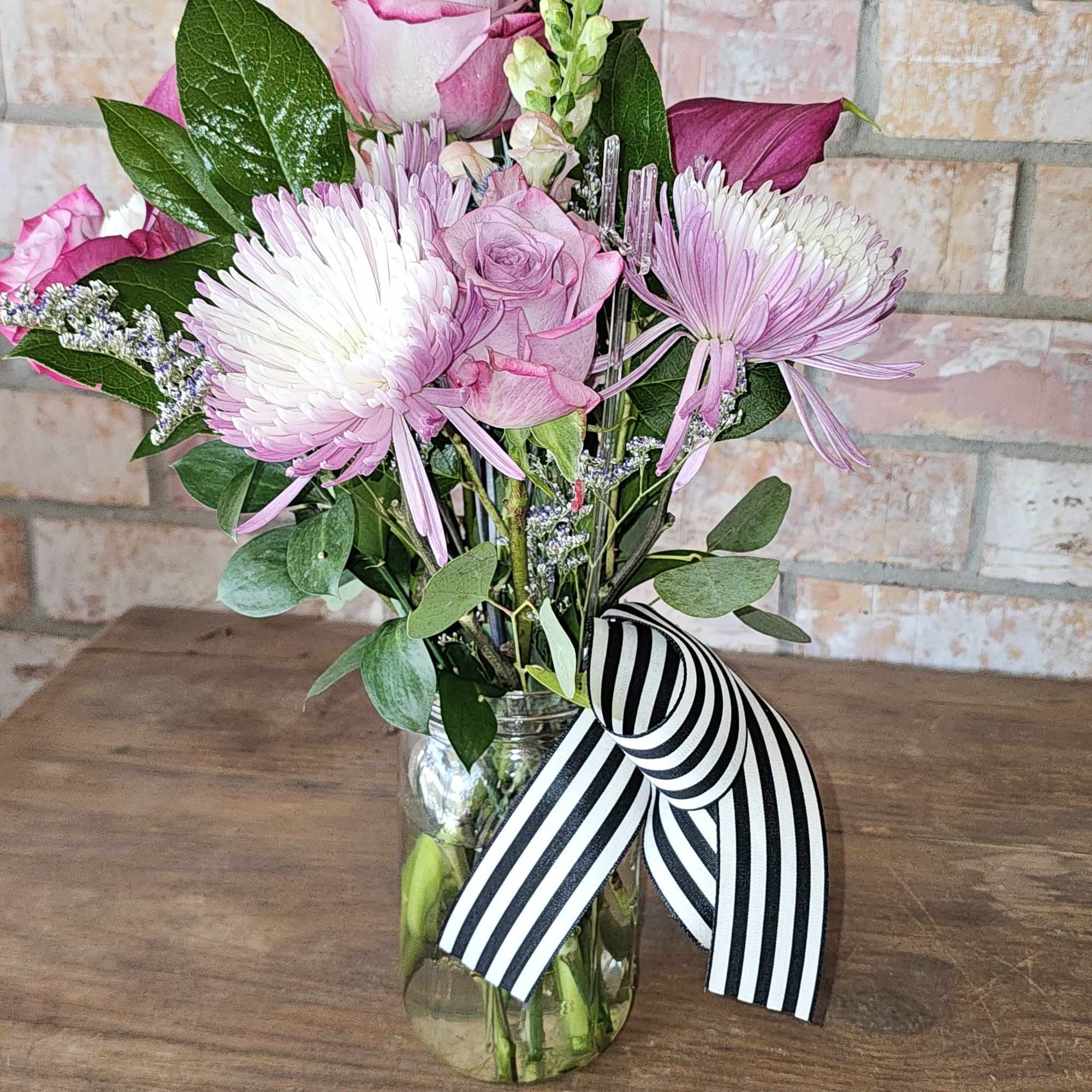 Pink roses and chrysanthemums in a glass jar with a striped ribbon