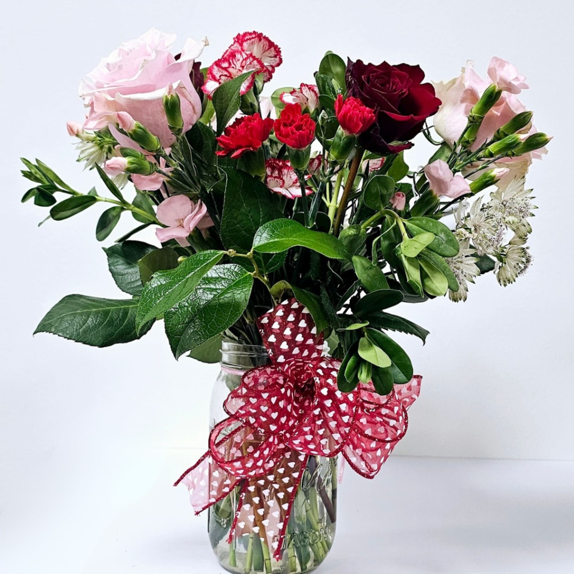 Bouquet of pink and red flowers in a glass jar with a heart ribbon