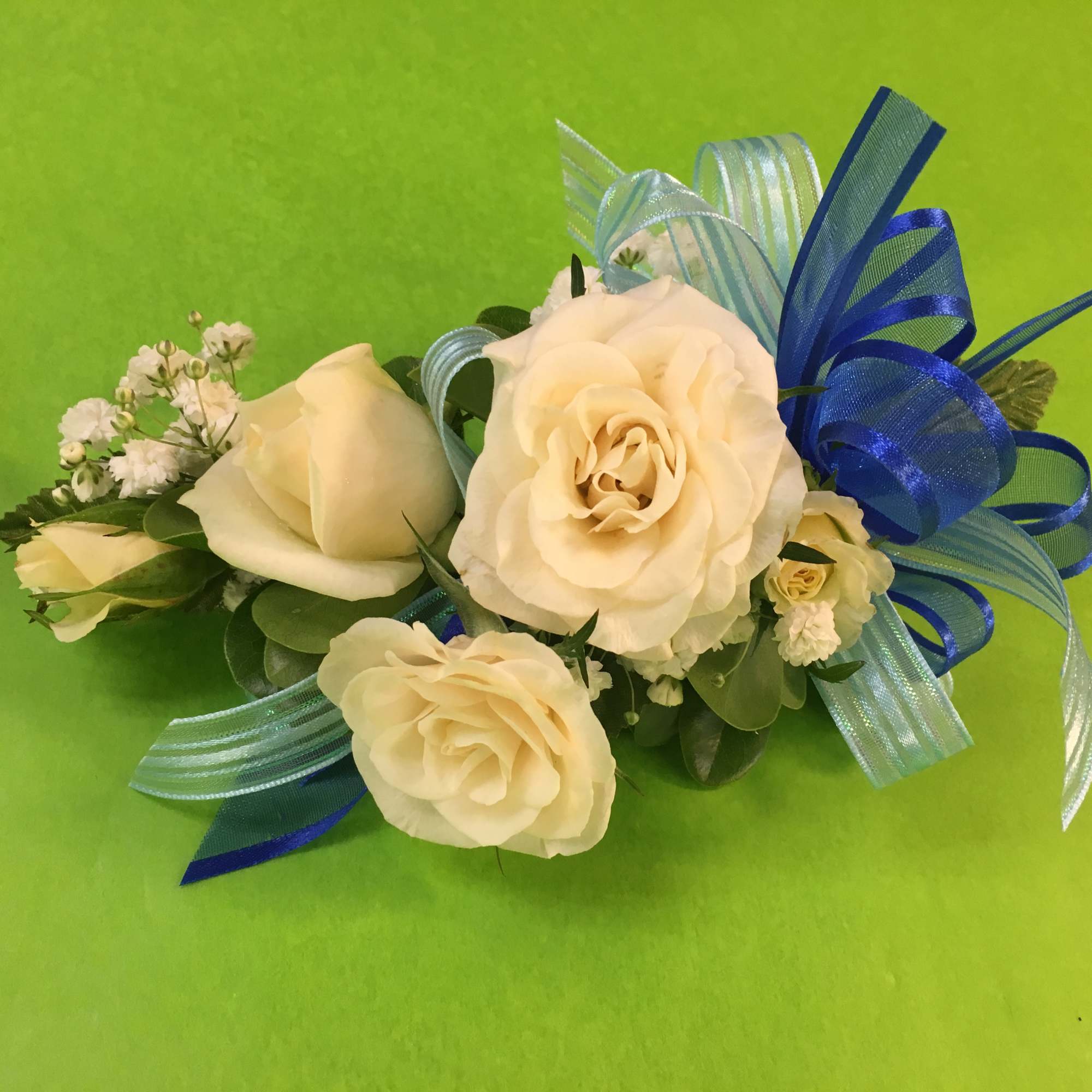 Cream rose corsage with blue ribbon on a green background