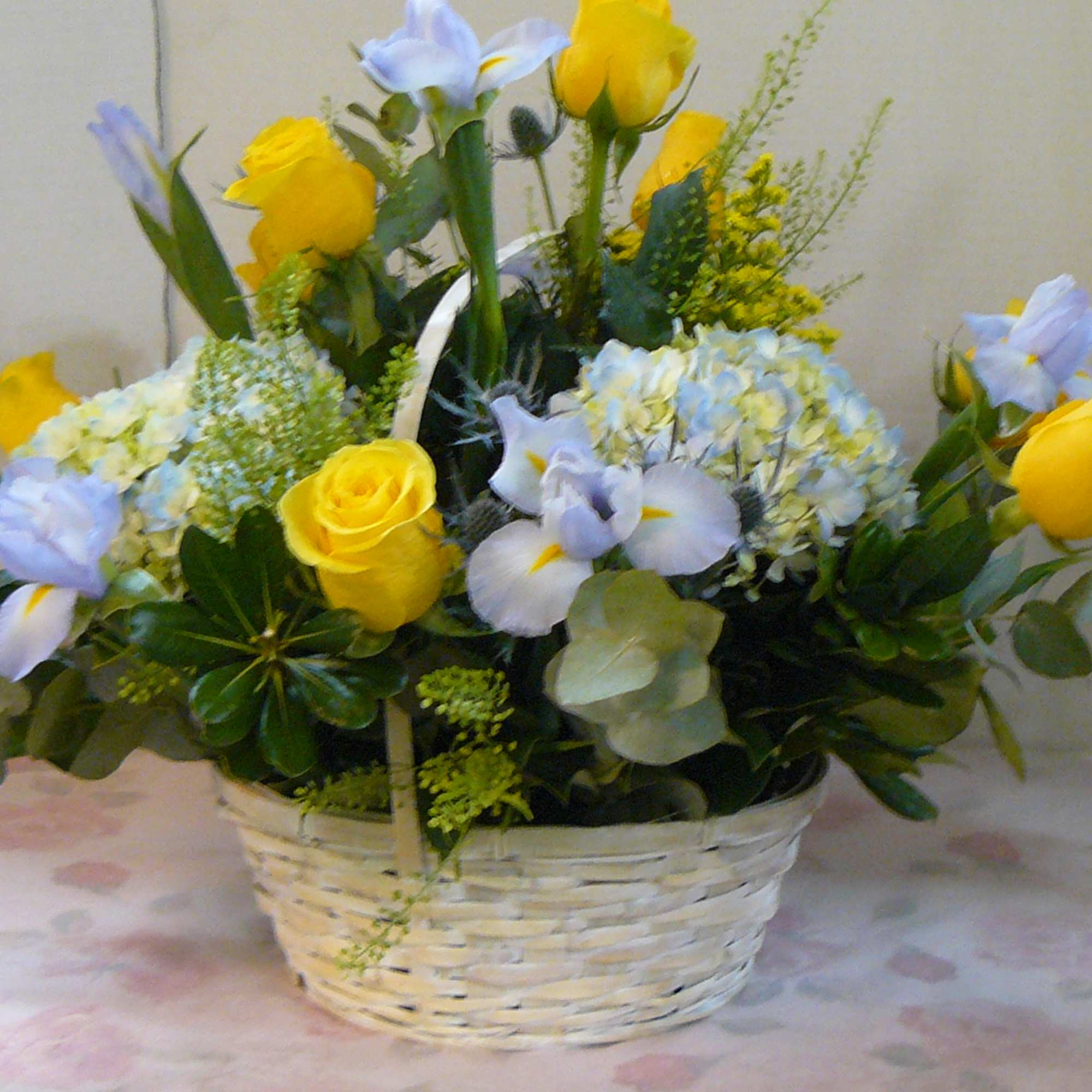 Basket arrangement of yellow roses and pale blue flowers