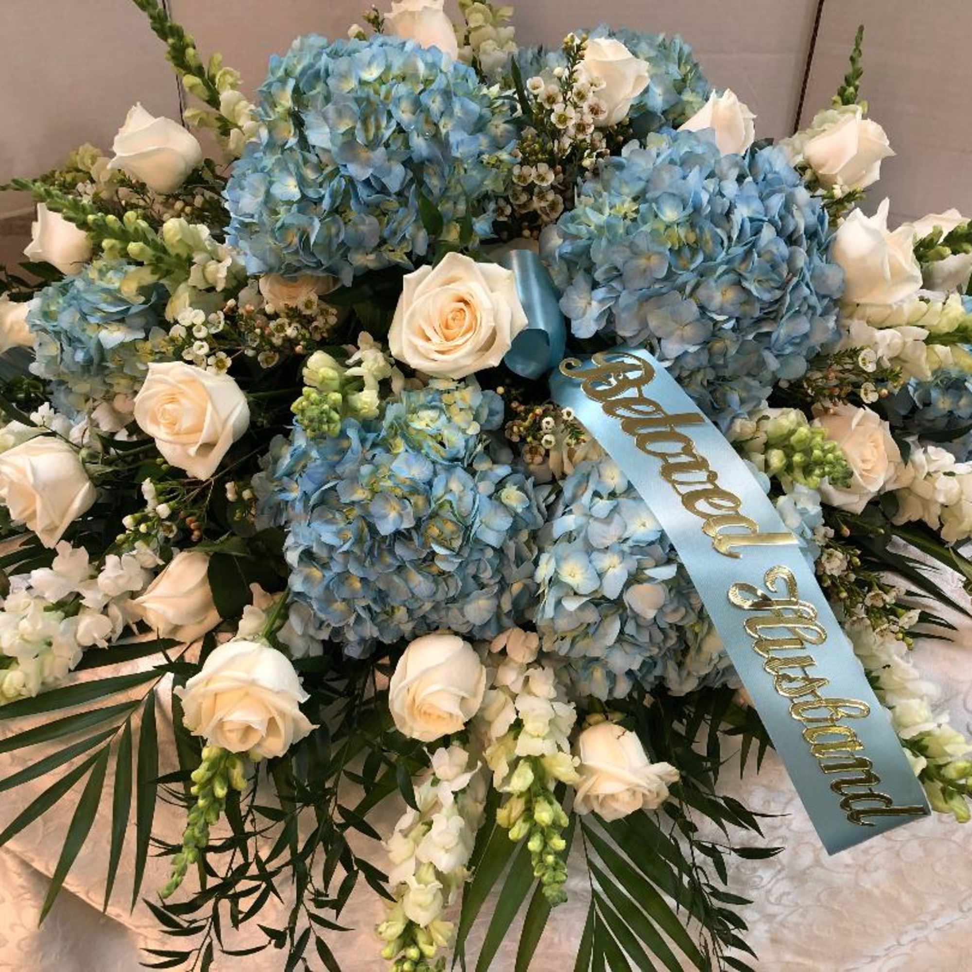 Blue hydrangea and white rose floral arrangement with a ribbon