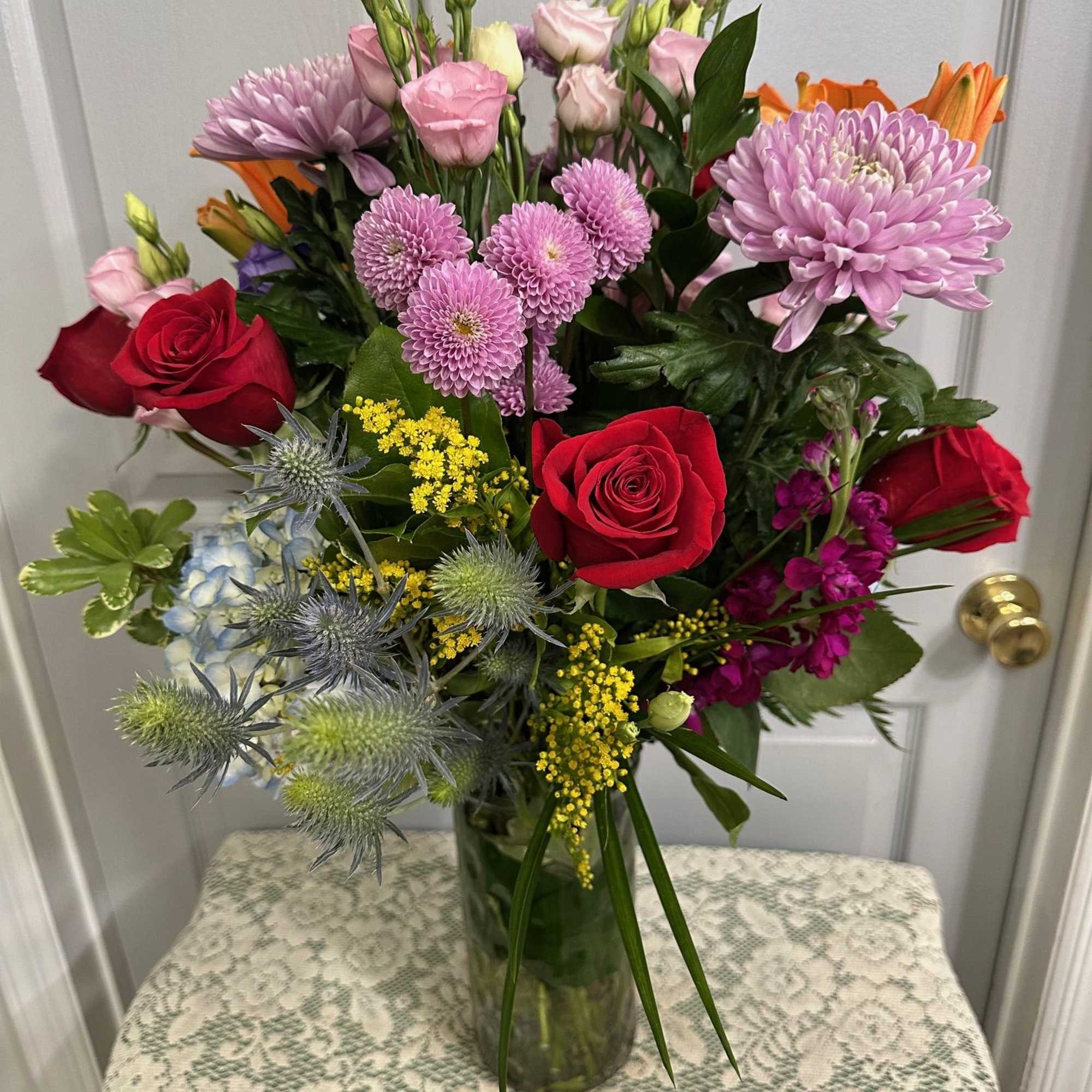 Mixed bouquet of red roses, pink blooms, and lavender flowers in a glass vase