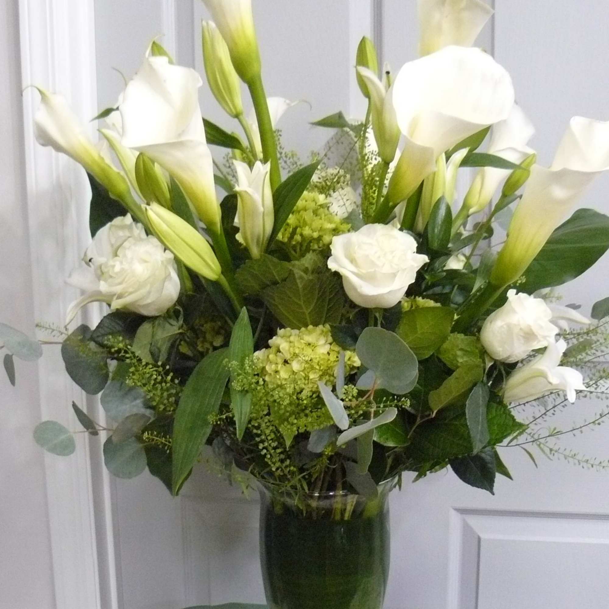 White calla lilies and roses arranged in a clear glass vase