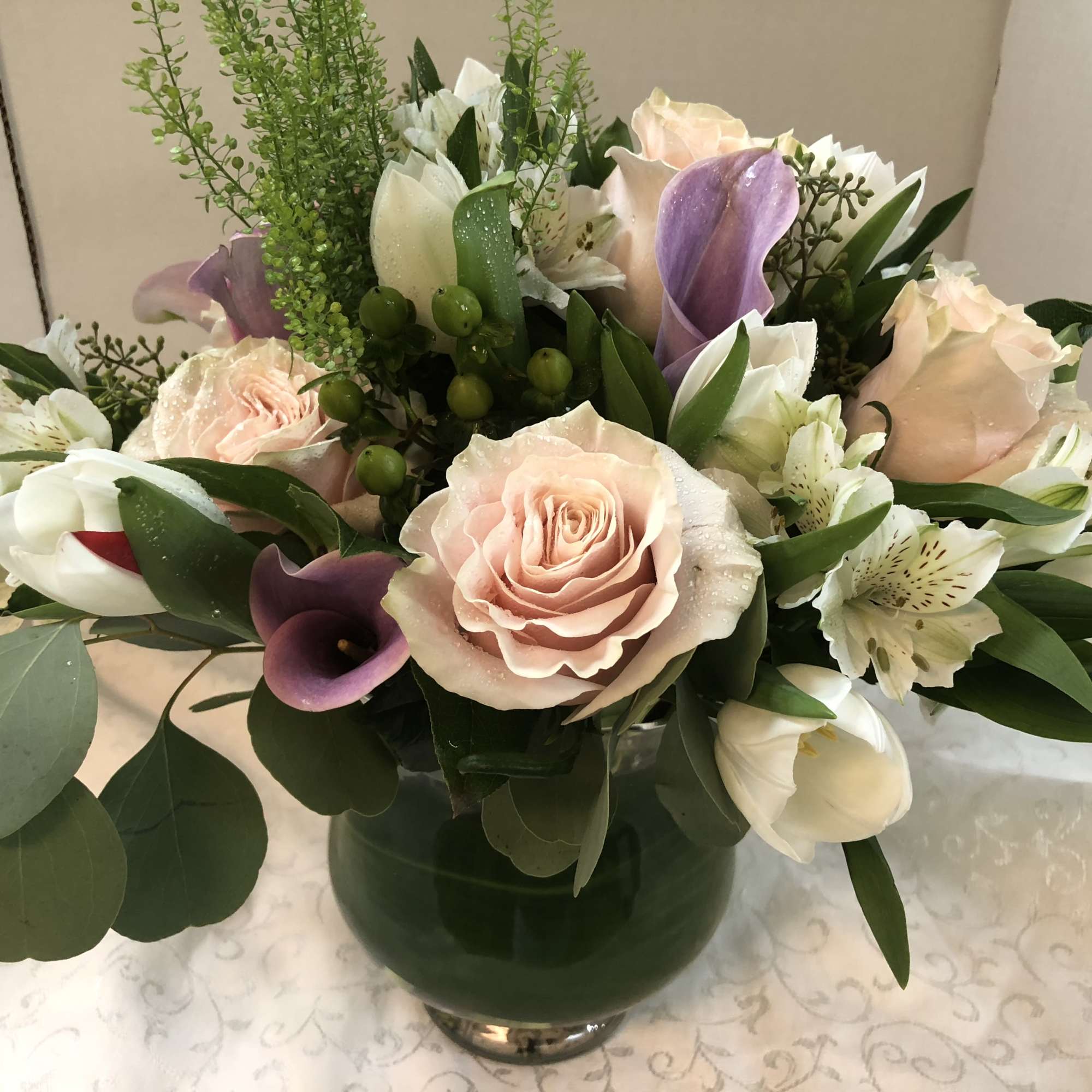 Bouquet of pale pink roses, white lilies, and purple calla lilies in a glass vase