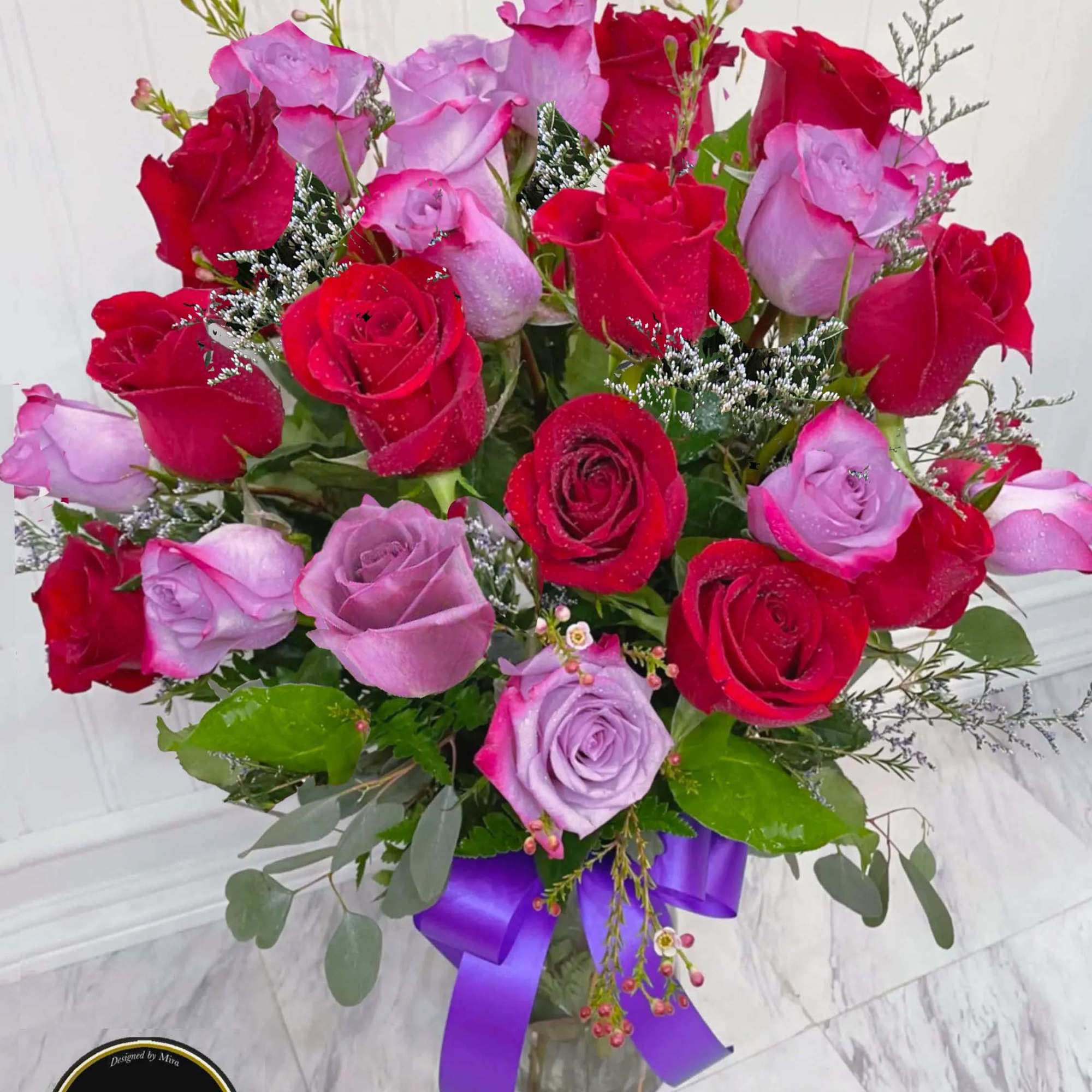 Arrangement of red and lavender roses in a clear vase with a purple ribbon bow