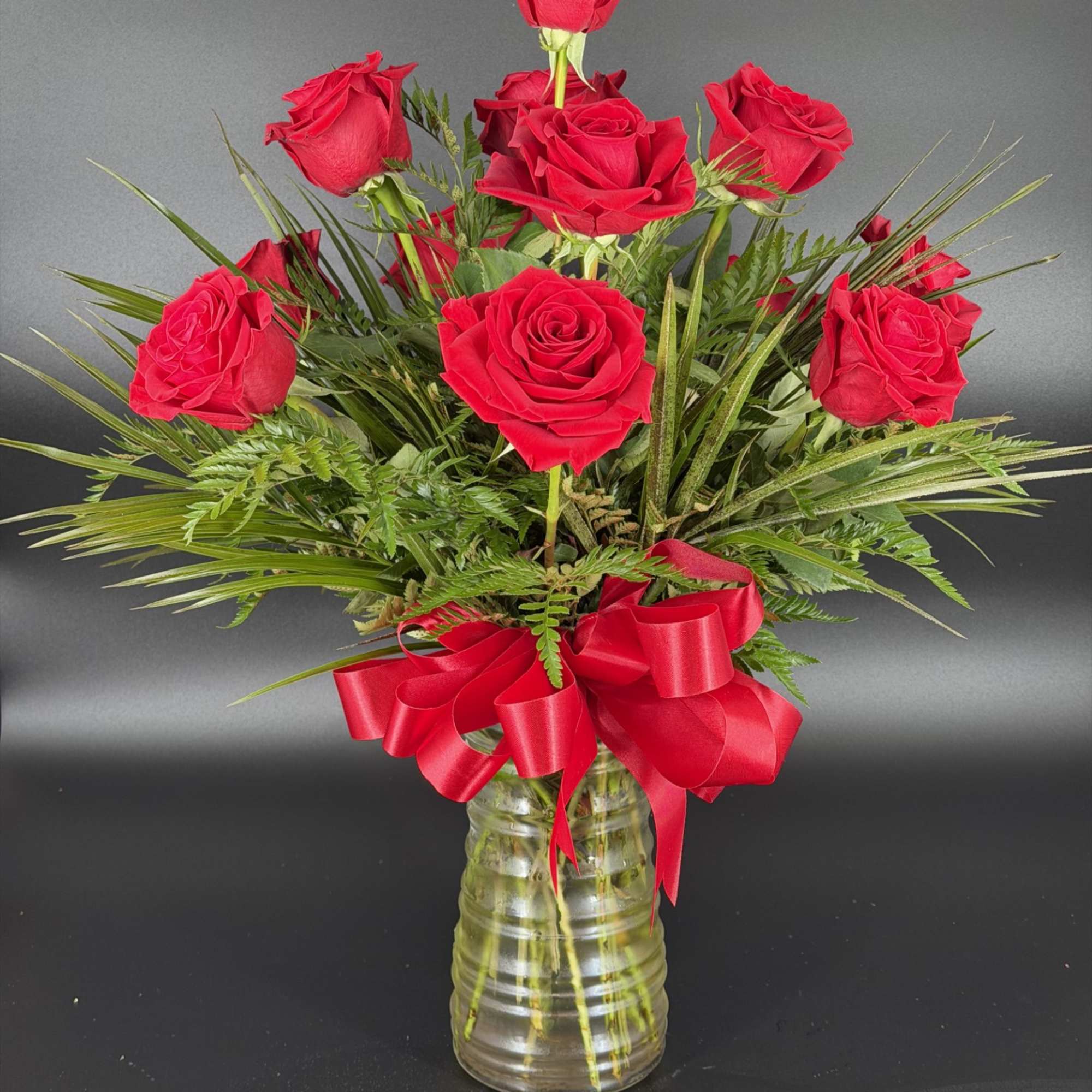 Red roses arranged in a clear glass vase with a red ribbon bow
