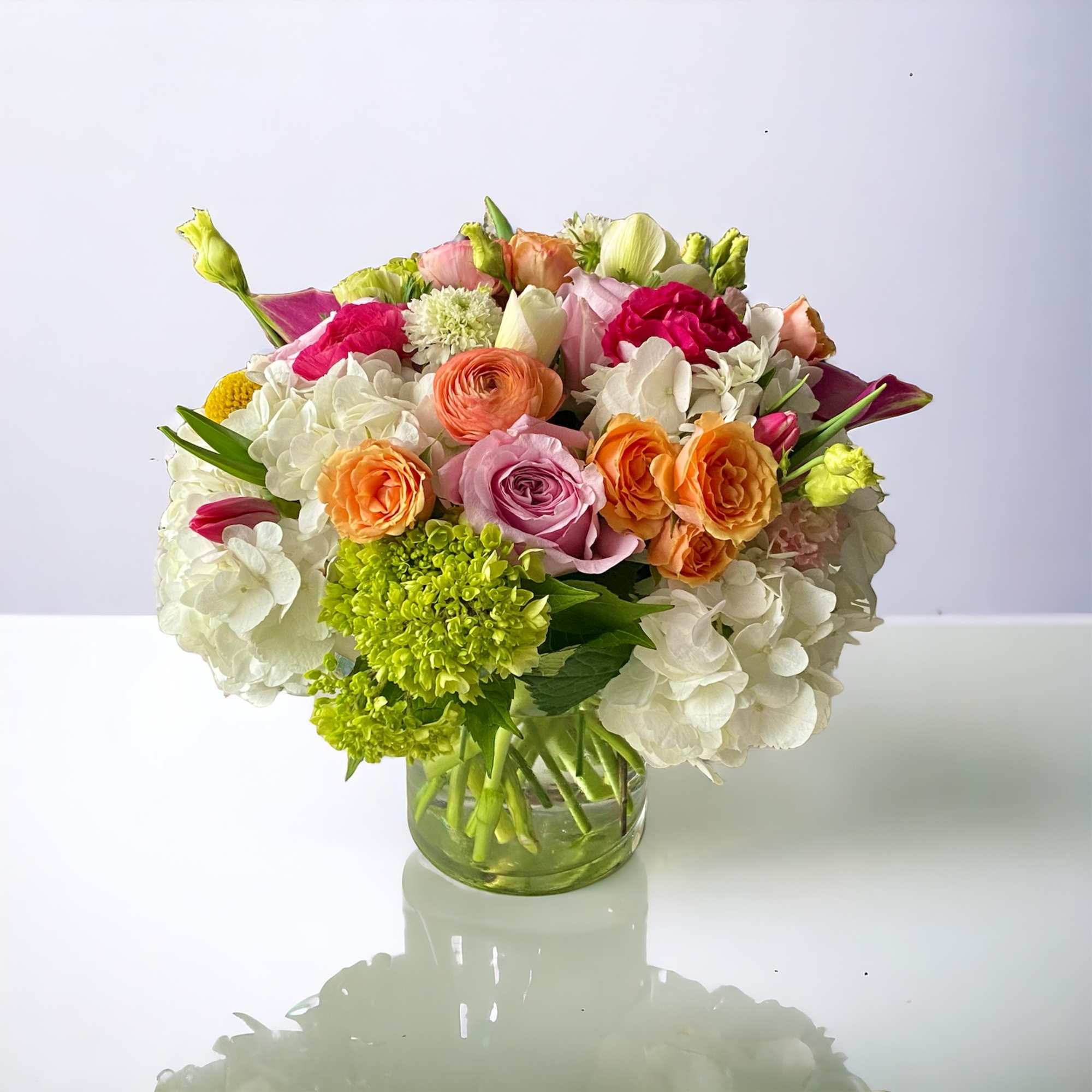 Mixed bouquet of pink, orange, white, and green flowers in a glass vase
