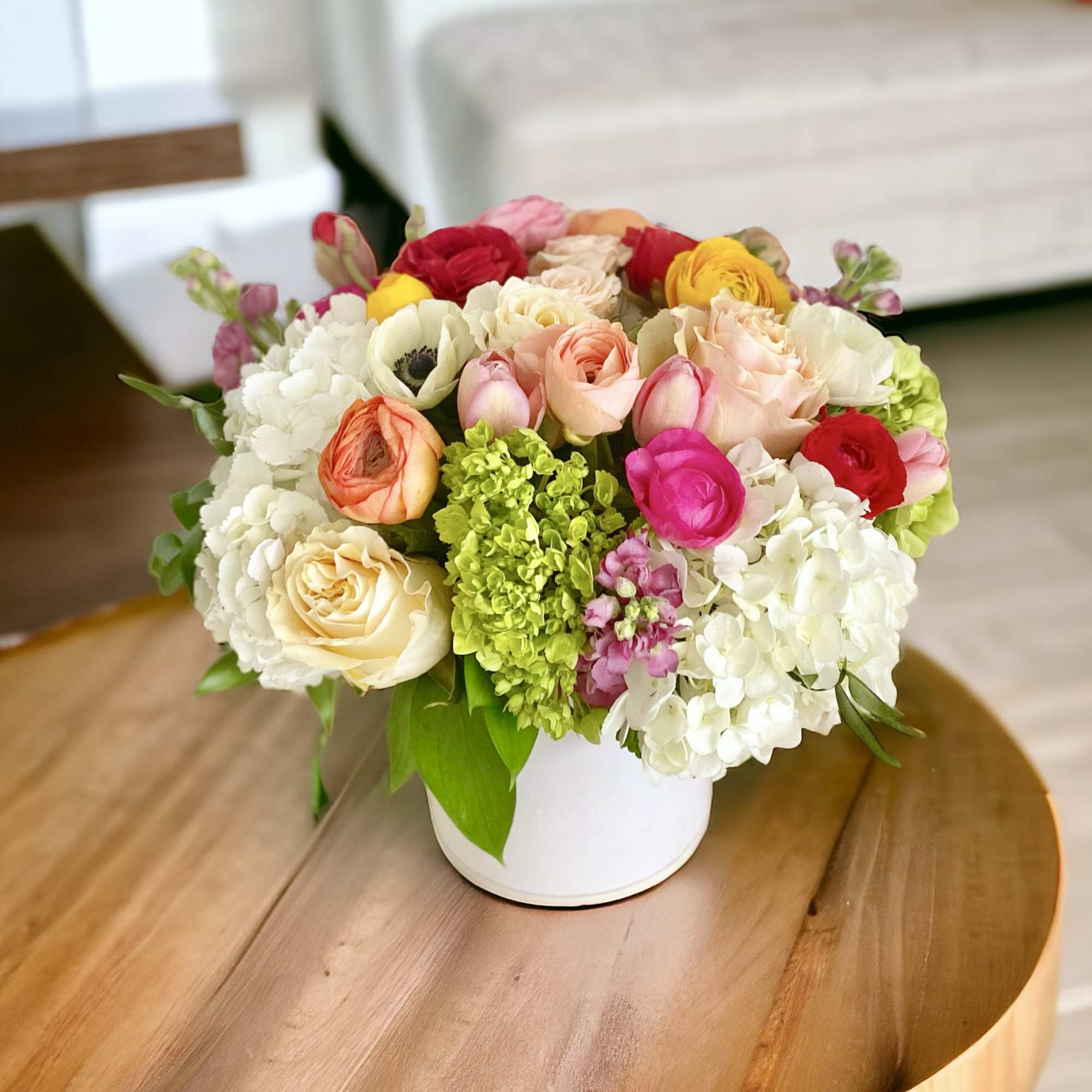 Mixed bouquet of roses, ranunculus, hydrangeas, and anemones in a white vase