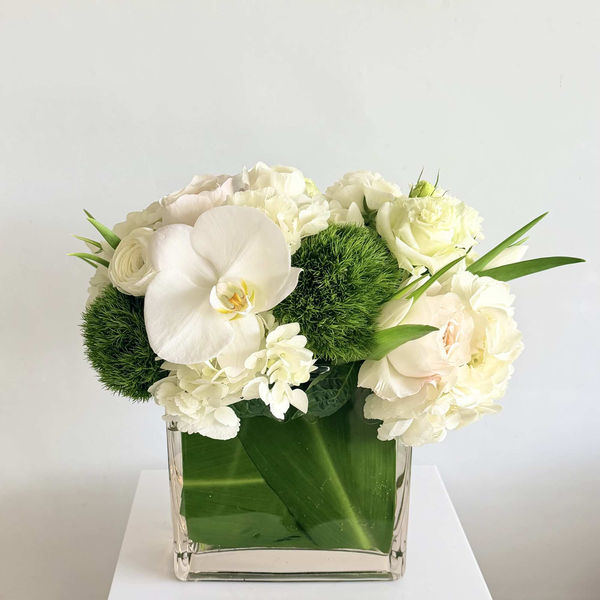 White floral arrangement in a clear square vase with green accents