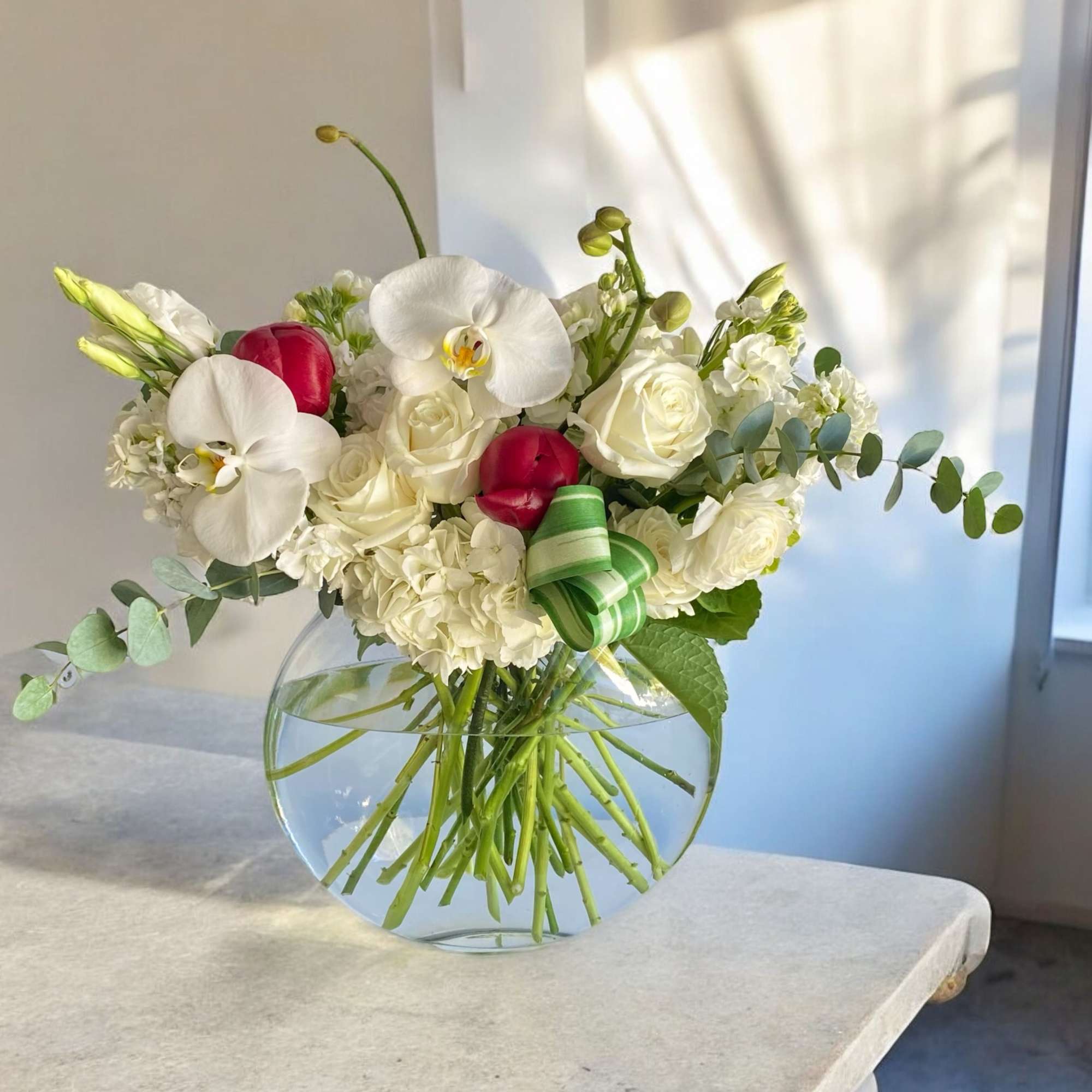 White floral bouquet with orchids and roses in a round glass vase