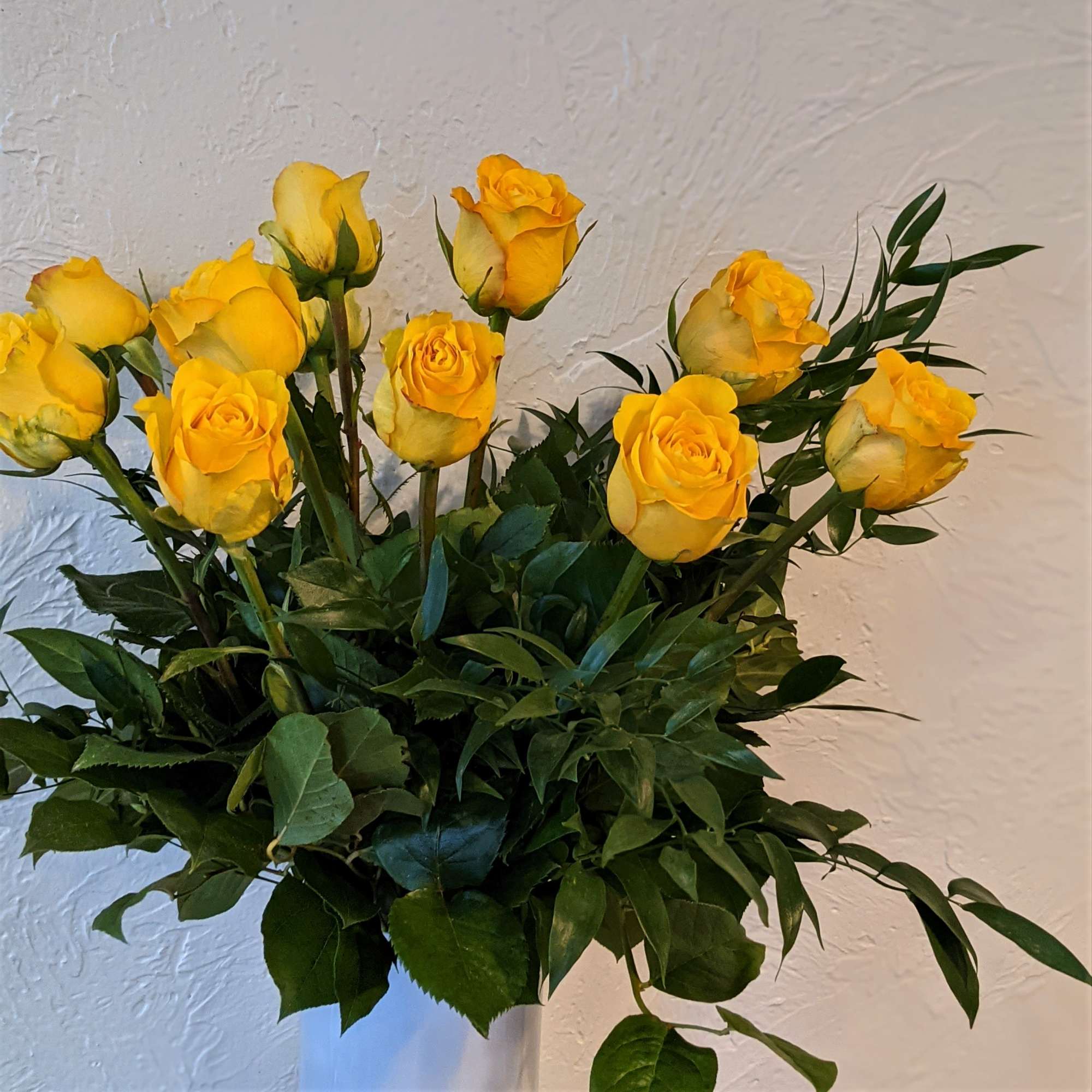 Yellow roses arranged in a white vase with dense greenery