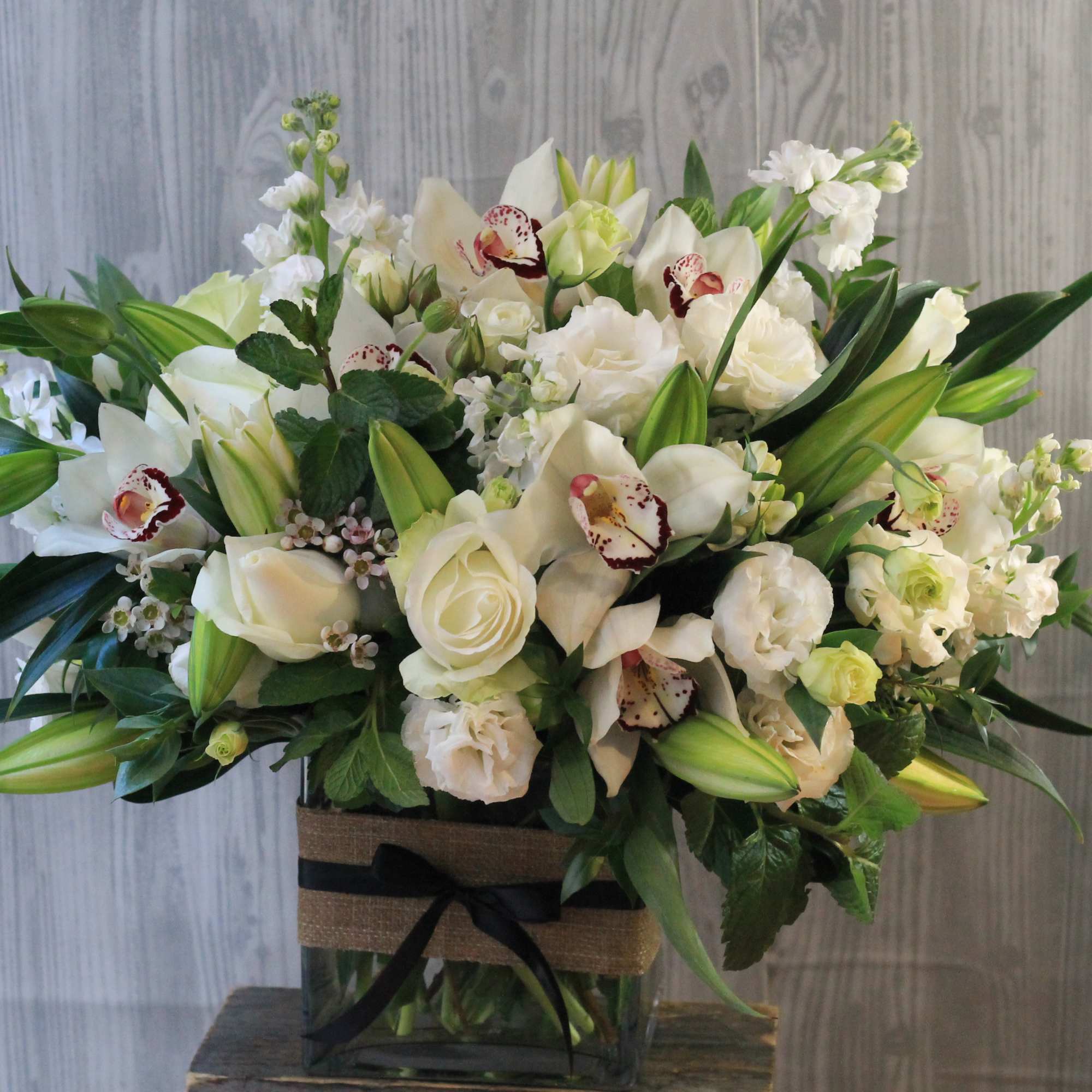 White floral arrangement in a square glass vase with a black ribbon