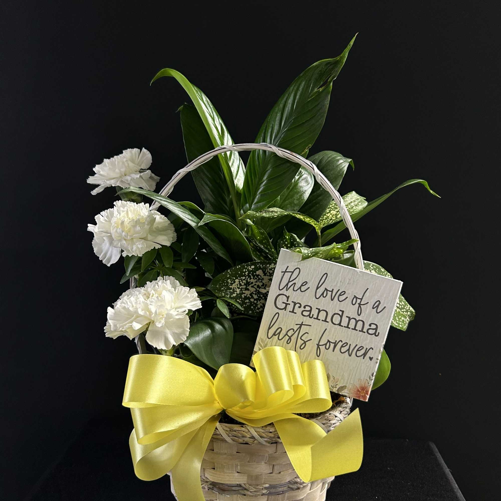 White carnations in a wicker basket with a yellow bow and a sympathy sign