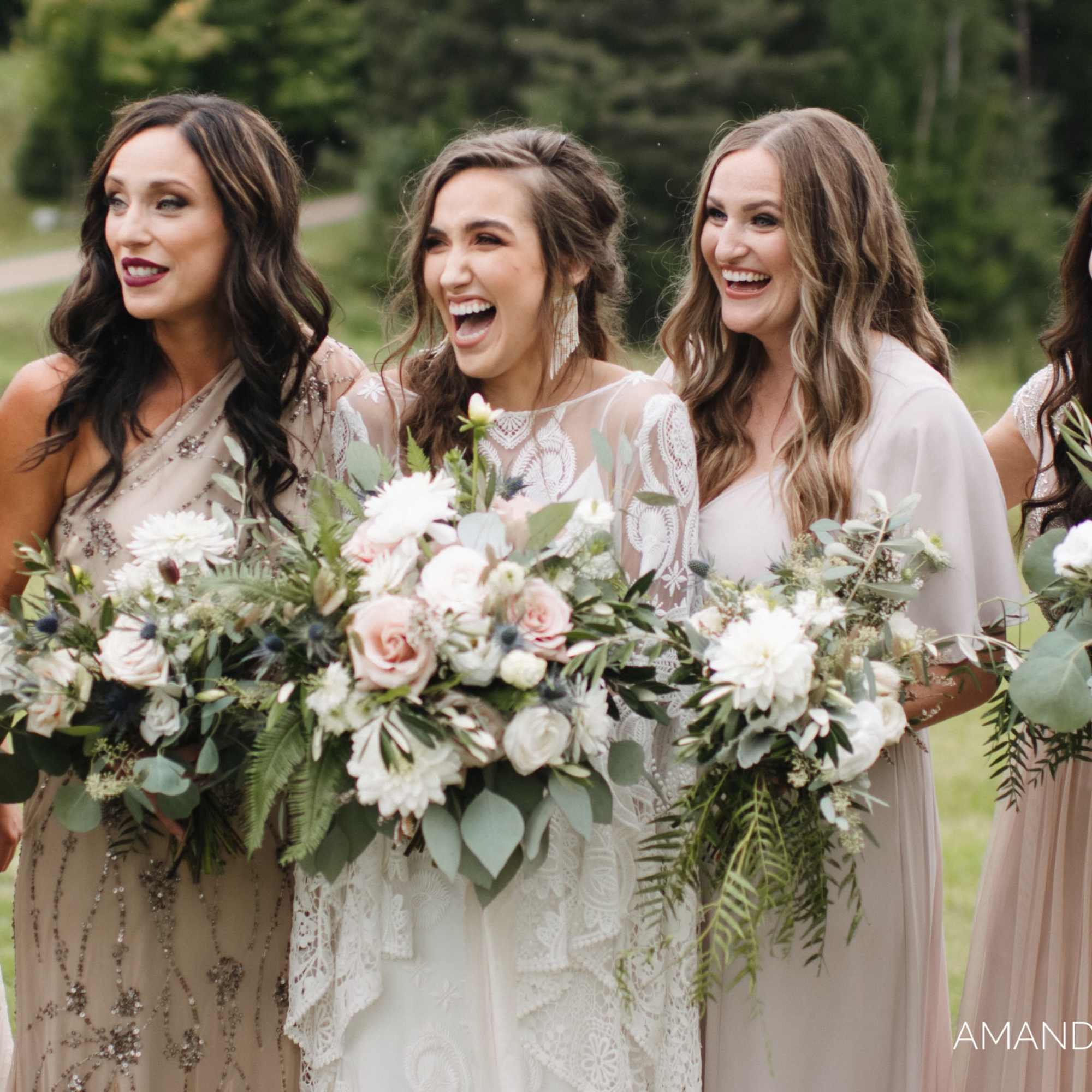 Five women in dresses holding large white and blush bouquets outdoors.