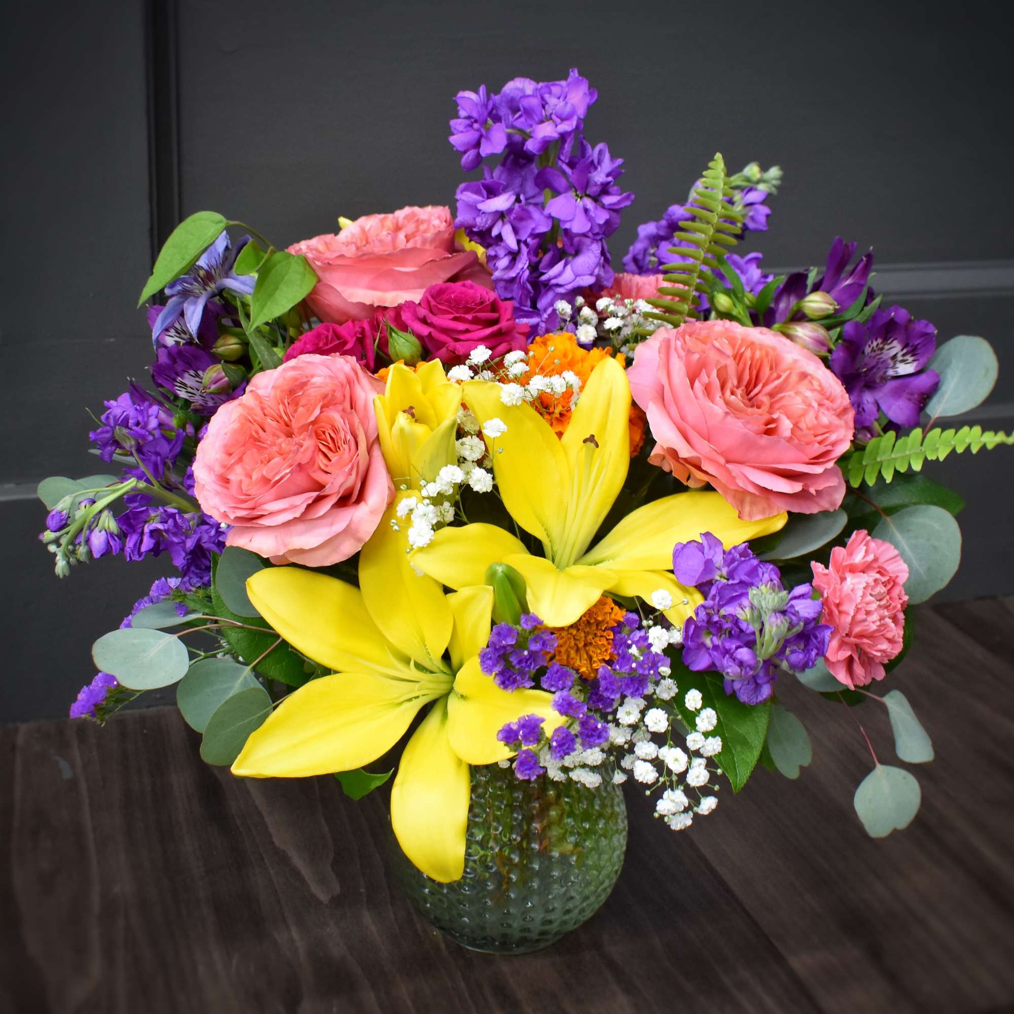 Bouquet of pink roses, yellow lilies, and purple flowers in a green vase