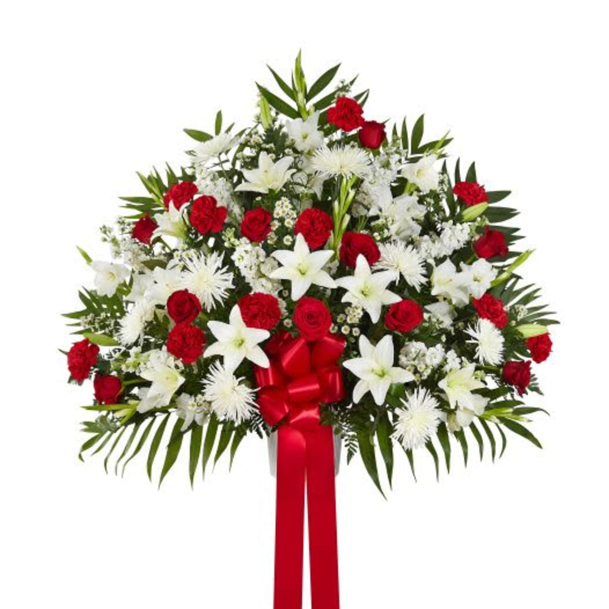 Standing spray of red roses and carnations with white lilies and mums, finished with a large red bow.