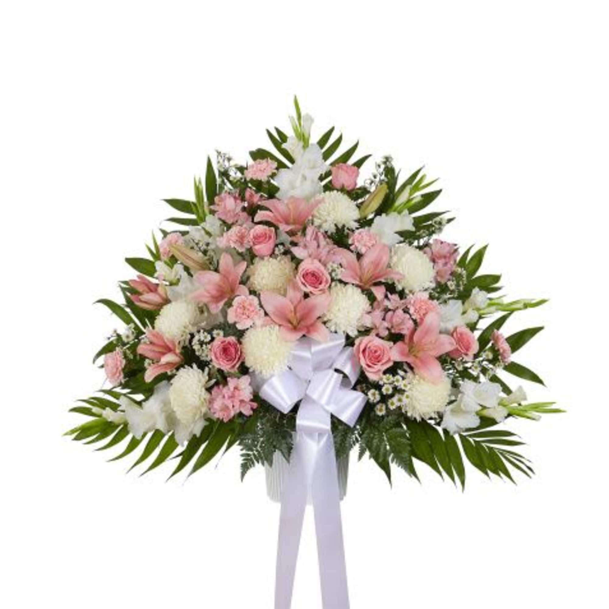 Fan-shaped arrangement of pink lilies and roses with white mums and a white bow in a white container