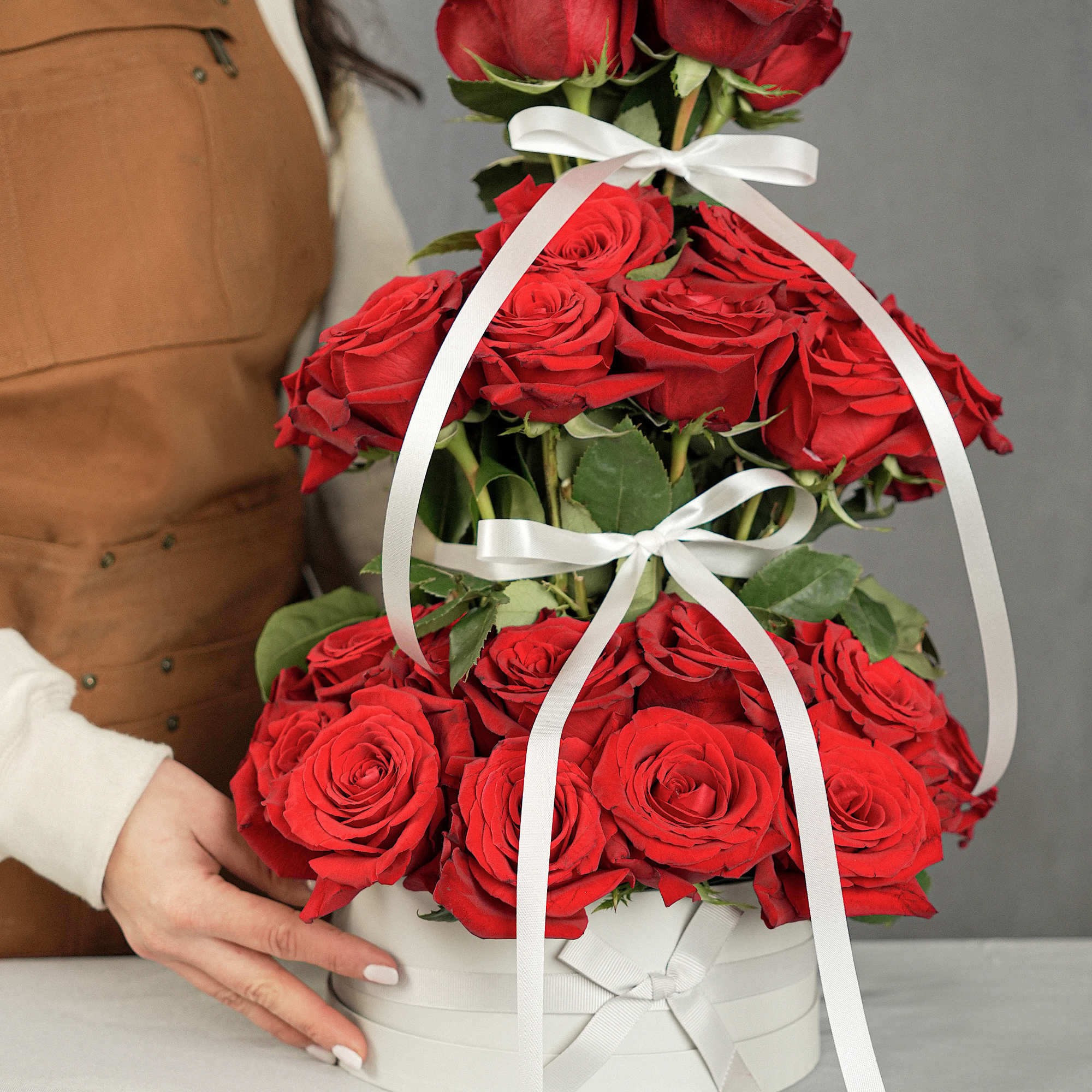 Tiered arrangement of red roses in a white hat box with ribbon