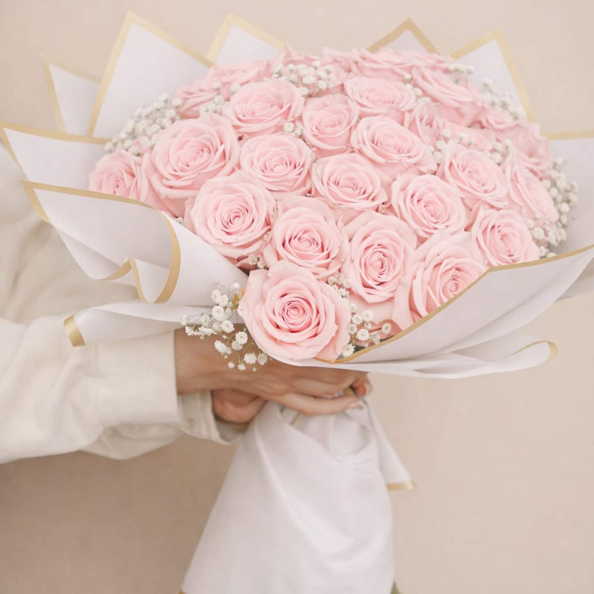 Bouquet of pale pink roses wrapped in white paper with gold trim