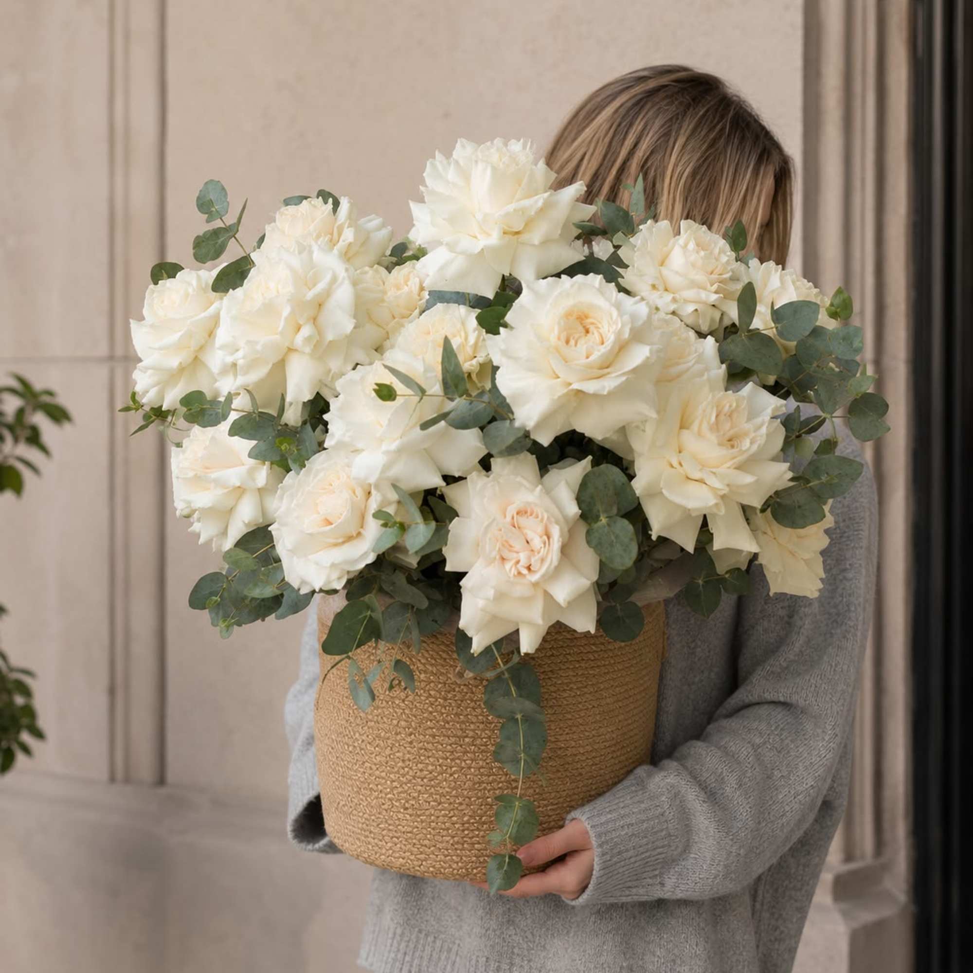 Large bouquet of white roses in a woven basket with eucalyptus