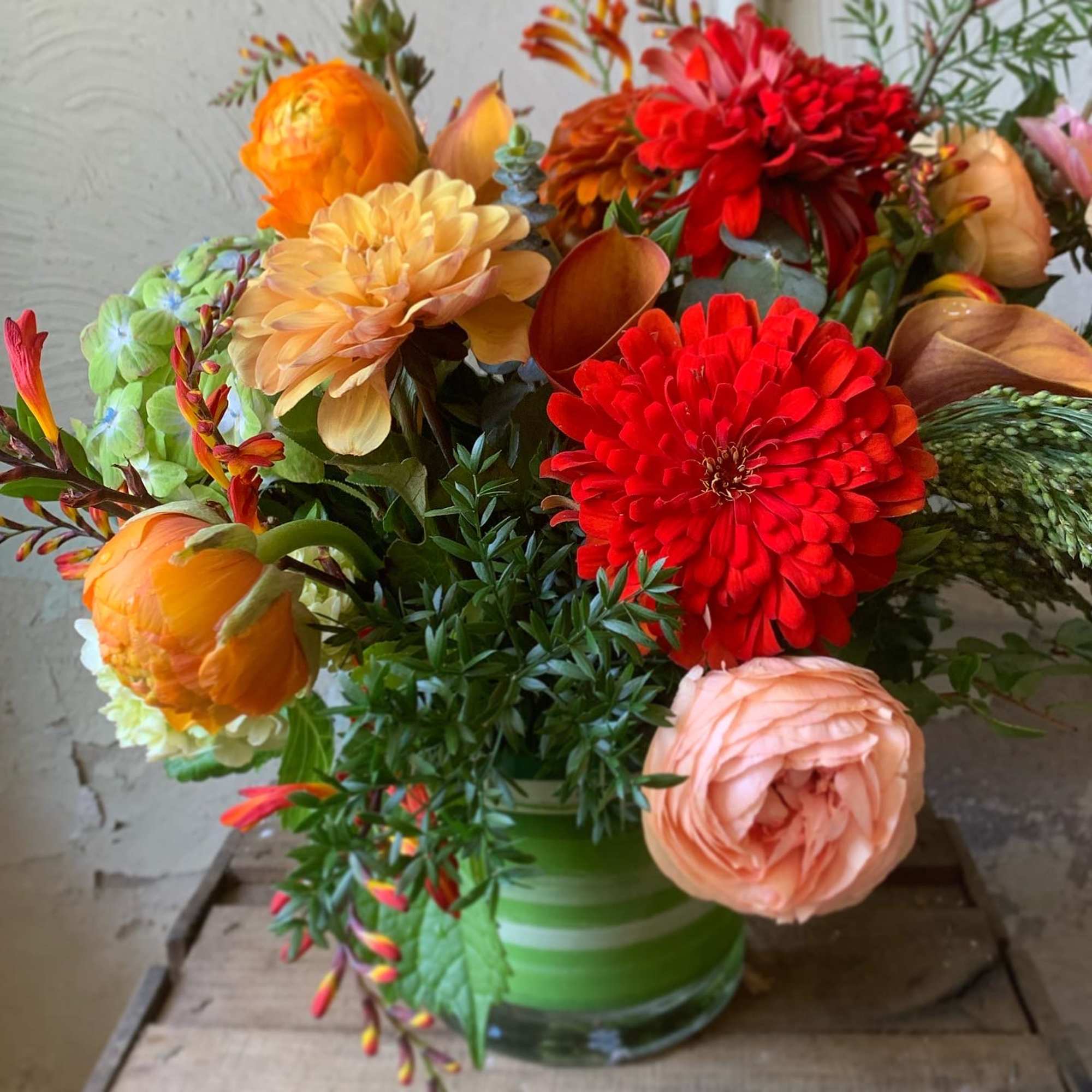 Colorful bouquet of orange, red, and peach flowers in a green glass vase