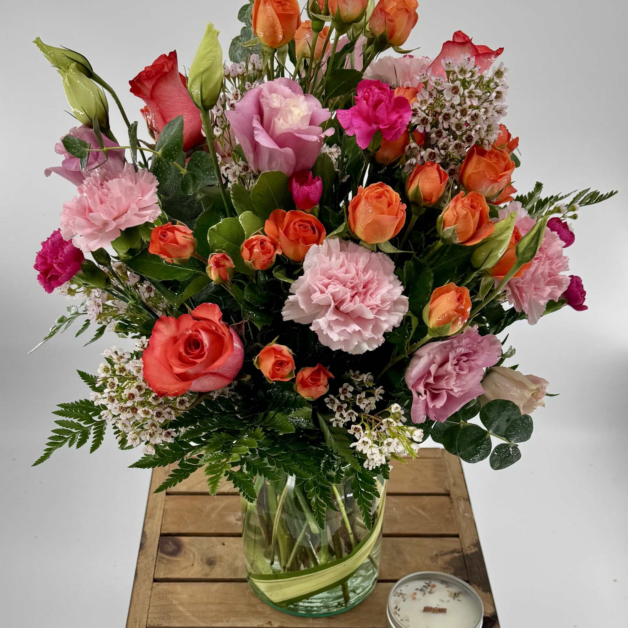 Mixed bouquet of roses and carnations in a glass vase with a candle