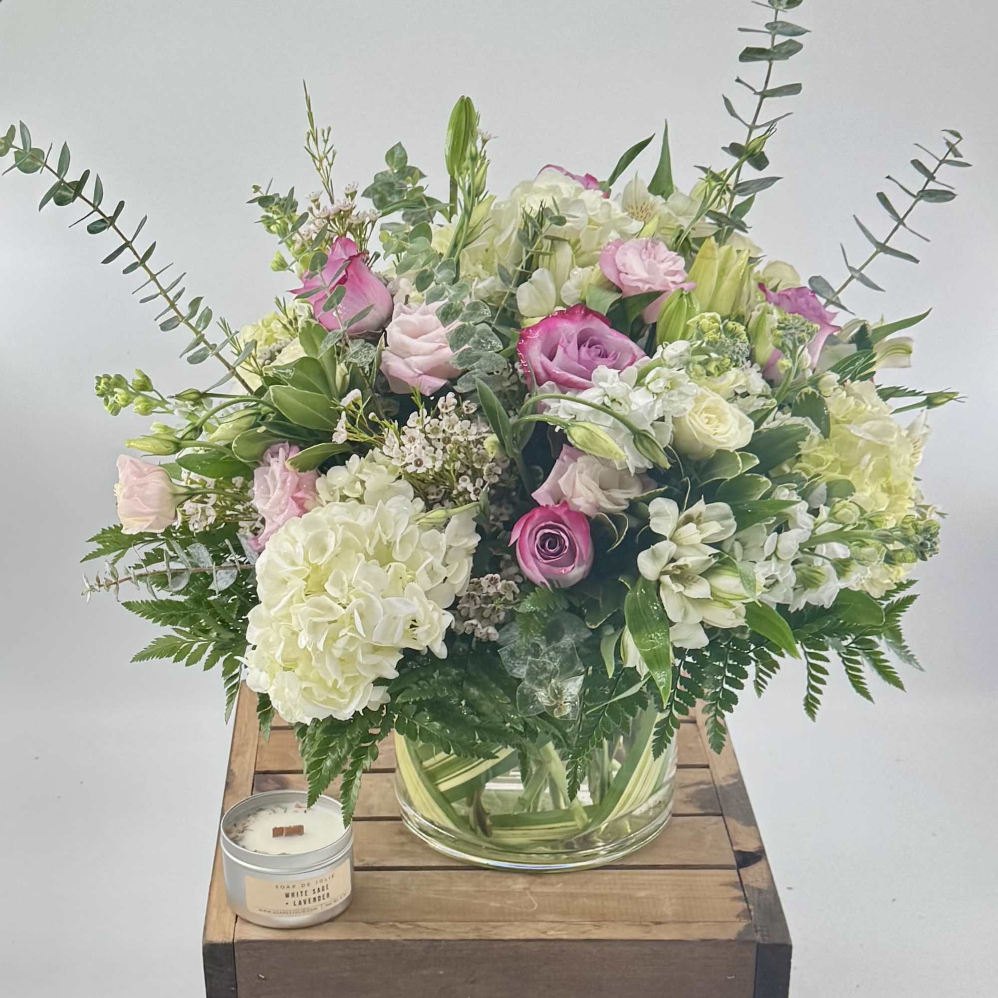 Pink and white floral arrangement in a glass vase with a candle beside it