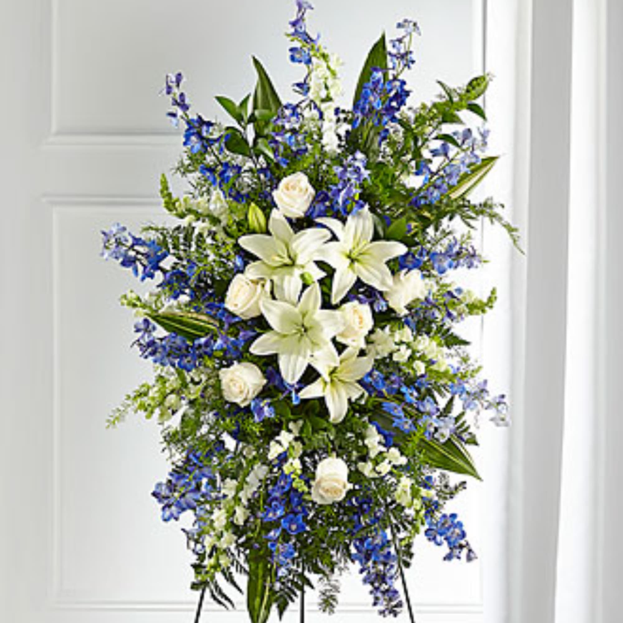 Tall standing spray of white lilies, white roses, and blue flowers