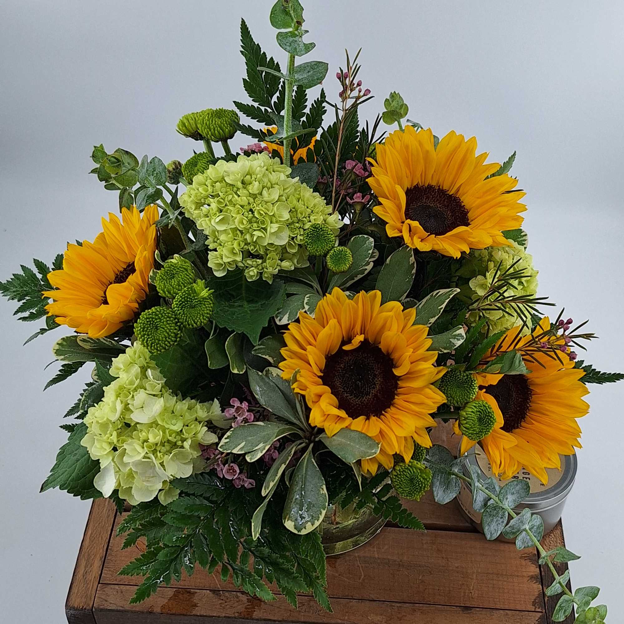 Sunflowers and green hydrangeas arranged in a low container with mixed greenery